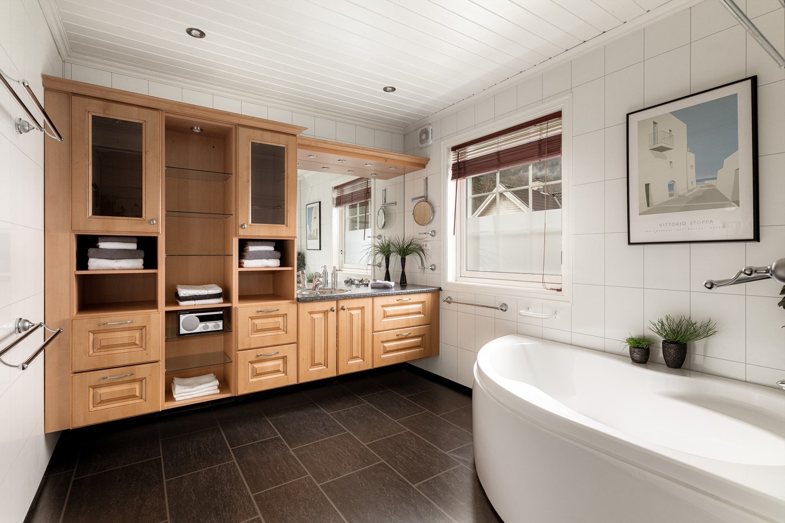 Badet i 1. etasje er fra 2006 og har belegg på gulv med varmekabler. Meget romslig innredning med god plass til oppbevaring i skuffer, skap og åpne hyller. Laminert benkeplate med nedfelt servant og speil med overlys. Galleribilde