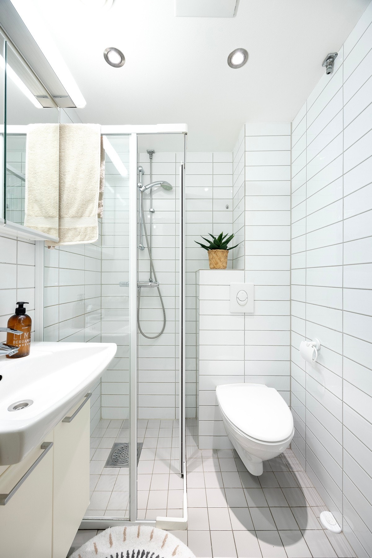 Flislagt baderom med vegghengt wc, servant med underskap, veggskap med speilfronter og dusjhjørne. Galleribilde