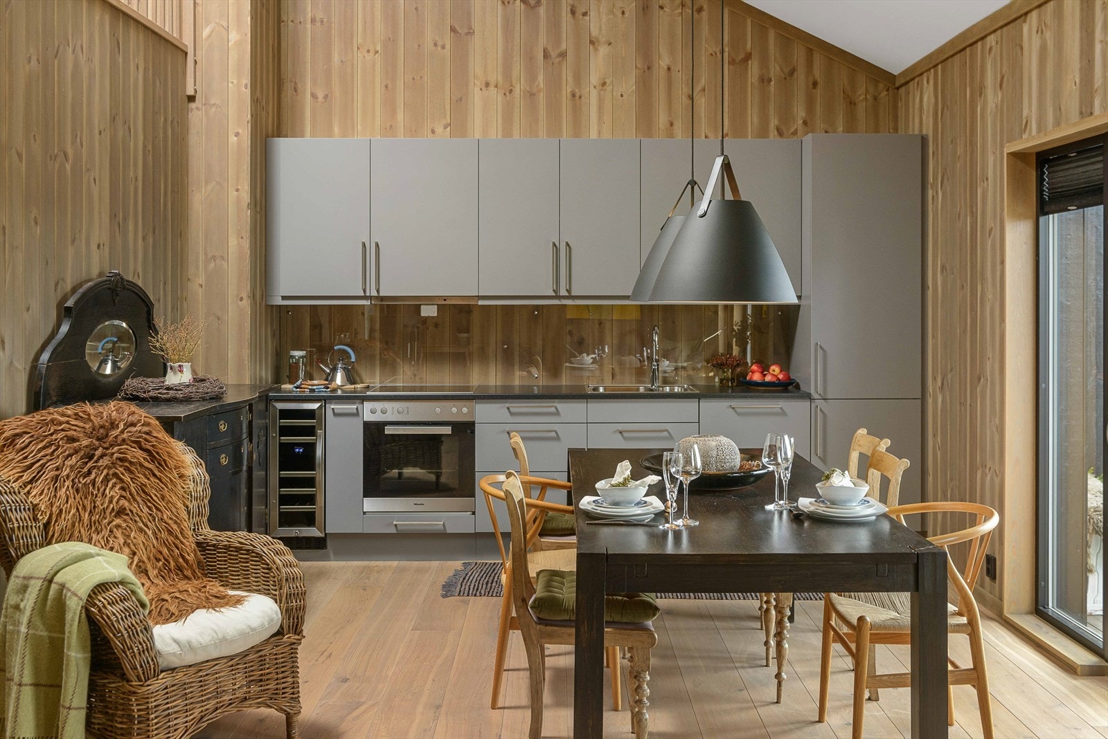 Stilrent kjøkken som er utstyrt med platetopp som er nedfelt i benk, stekeovn med kjøkkenvifte over, oppvaskmaskin, kjøle-/fryseskap og vinskap som er integrert i innredningen. Galleribilde