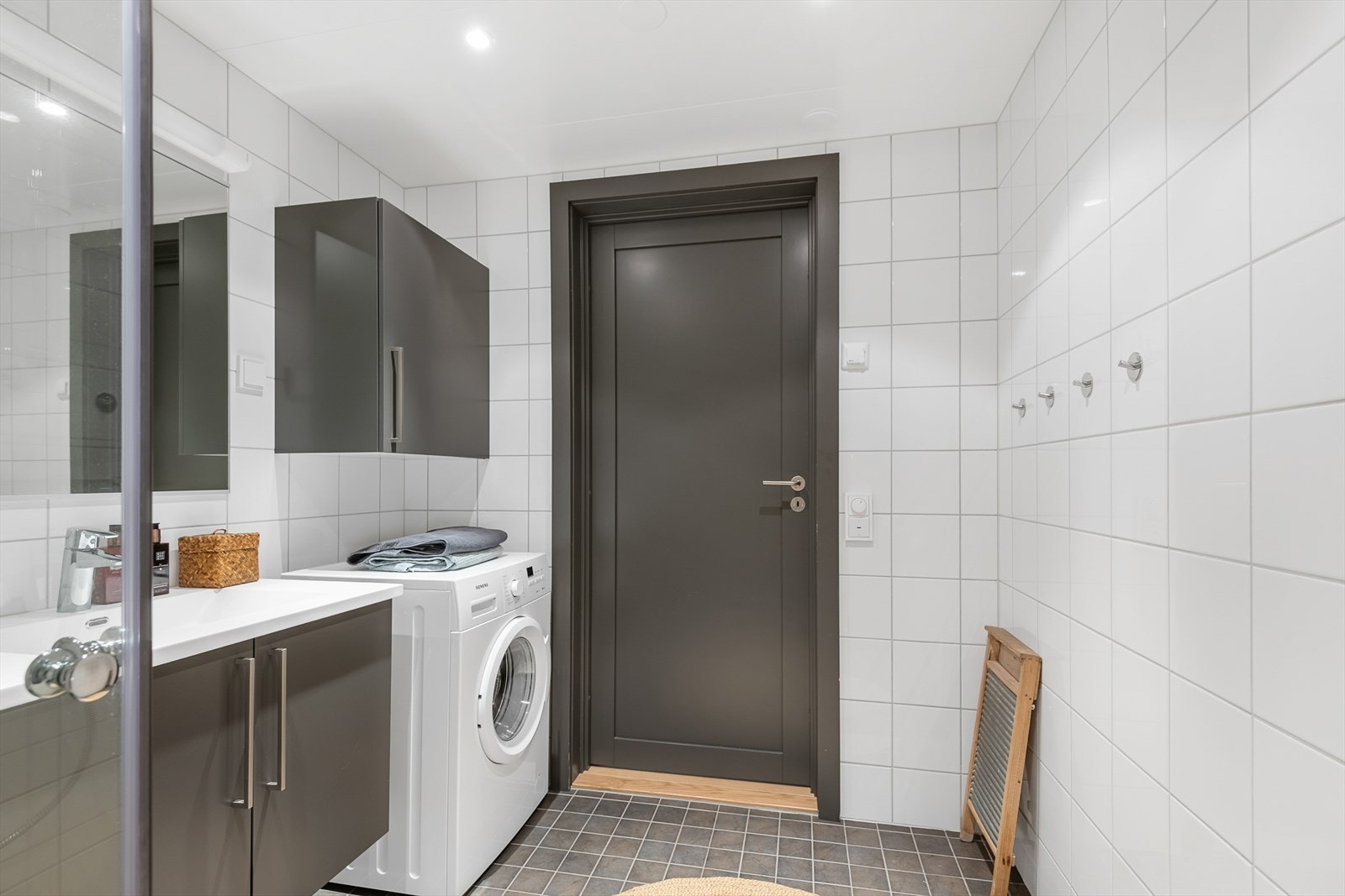 Badet er utstyrt med vegghengt toalett, dushjørne med glassdører, heldekkende servant på baderomsinnredning med speil og lys over samt opplegg til vaskemaskin med skap på veggen over. Galleribilde