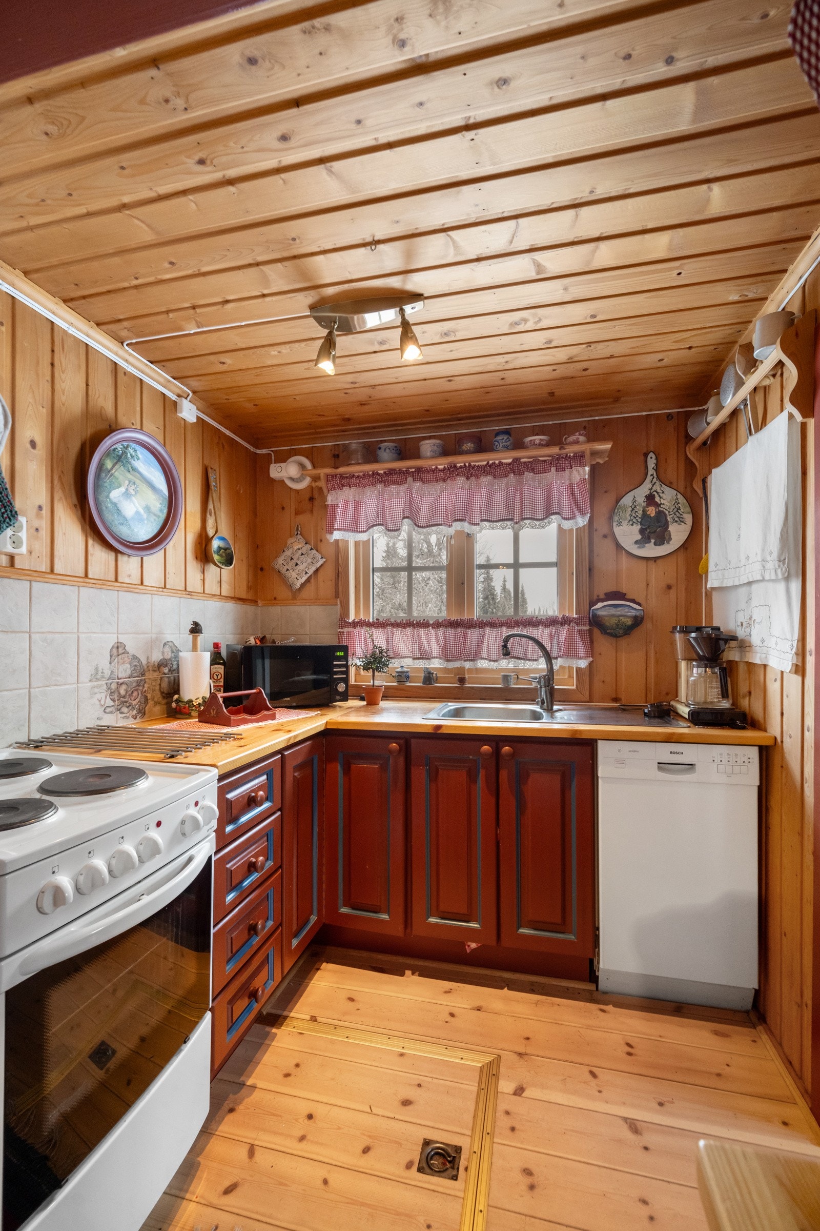 Kjøkkenet er praktisk utformet med plass til både vedovn, en liten oppvaskmaskin og en komfyr, og det er god benkeplass til matlaging og forberedelser Galleribilde