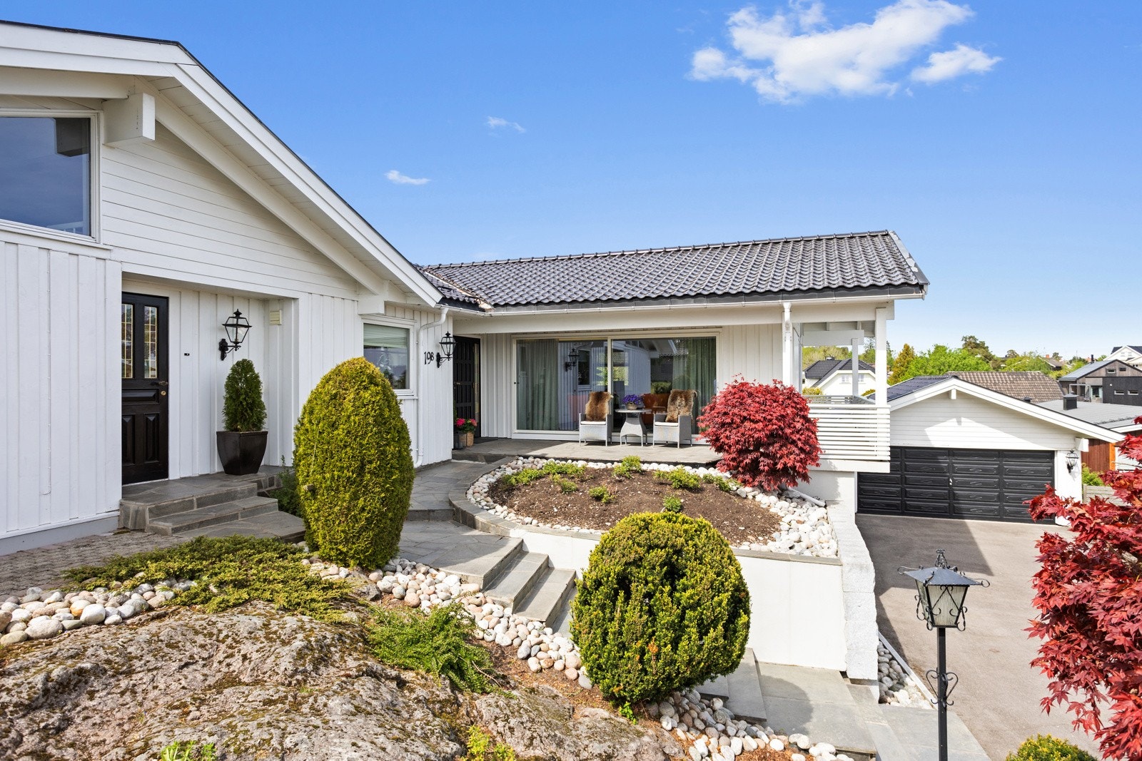 Tomten har store og fine blomsterbed og steinalgte veier mellom uteplassene. Skifertrappen opp til ytterdøren har varmekabler. Galleribilde