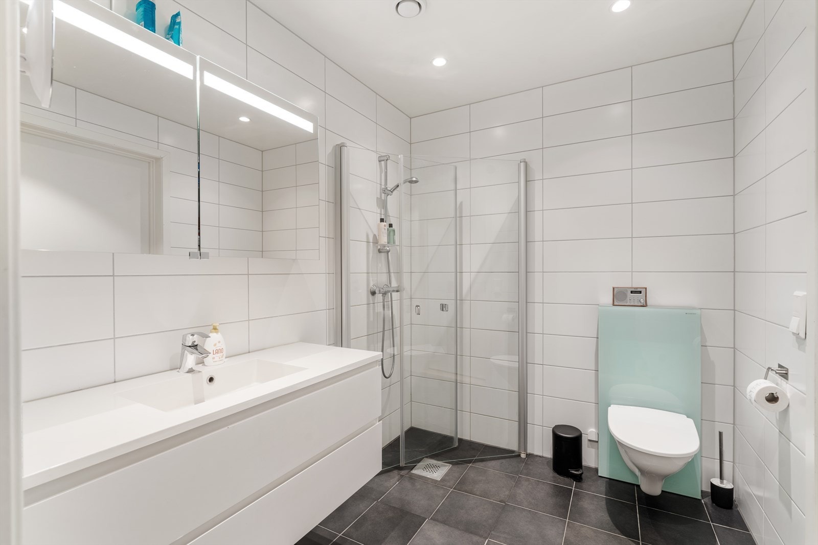 Helfliset bad i 1. etasje med vegghengt toalett, vask i møbel og dusjnisje Galleribilde