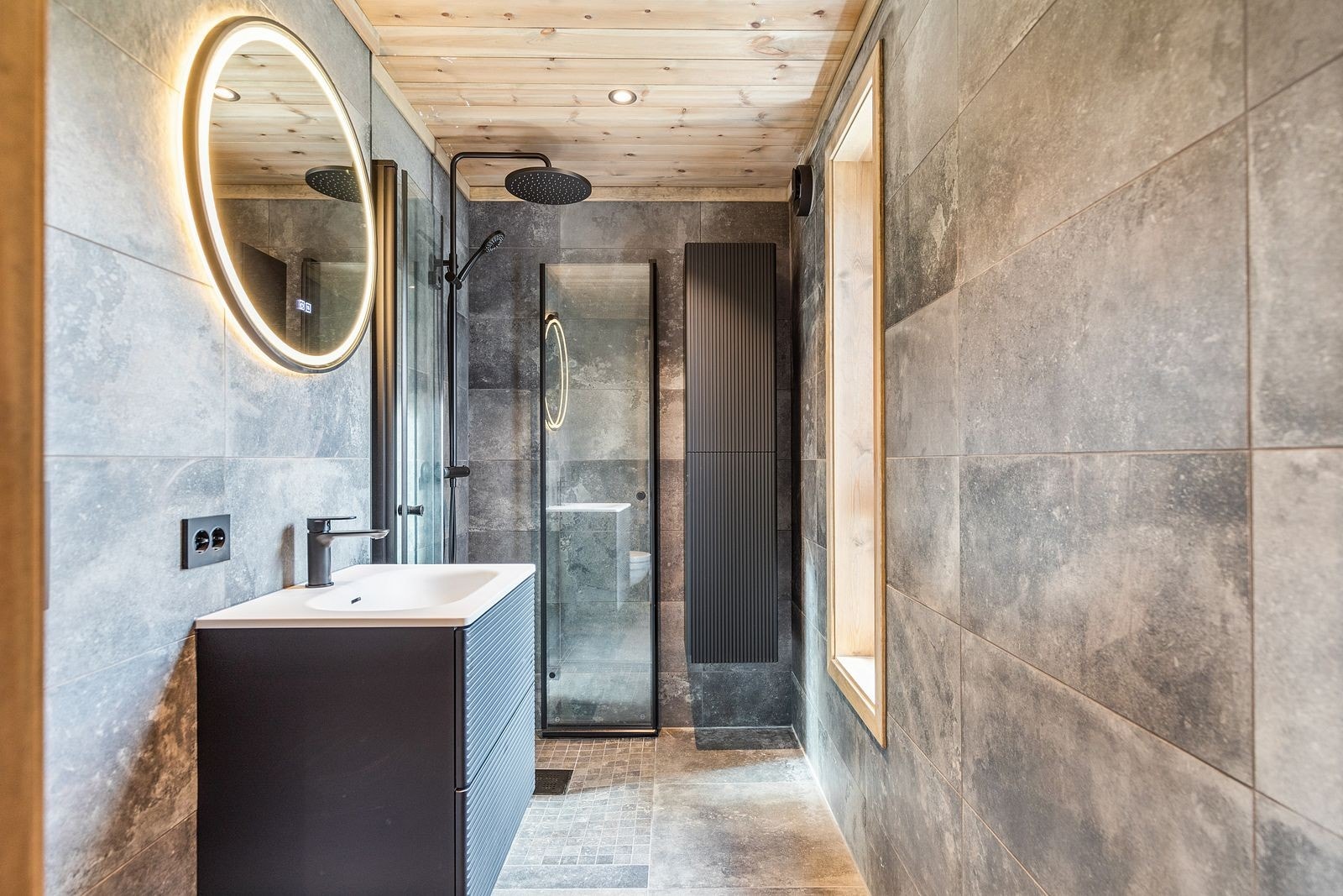 Stilfullt flislagt bad med varmekabler i gulv, vegghengt wc vannfalldusj og innskyvbare dusjdører. Galleribilde