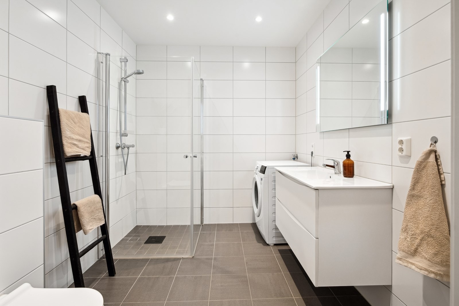 Flislagt baderom med gulvvarme. Badet har hvit glatt innredet med servant i baderomsinnredning, vegghengt toalett og dusj. Galleribilde