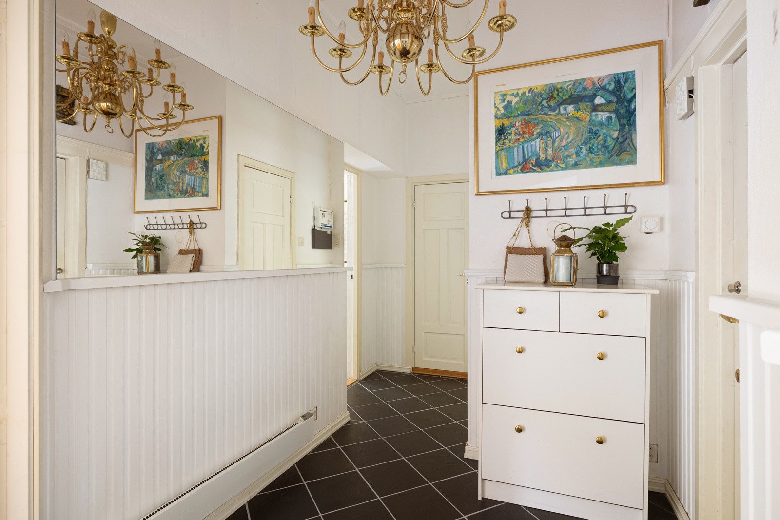 Du ønskes velkommen inn i en lys og praktisk entré med mørke fliser på gulvet, lyse overflater og et bredt speil som gir rommet ekstra dybde. Galleribilde