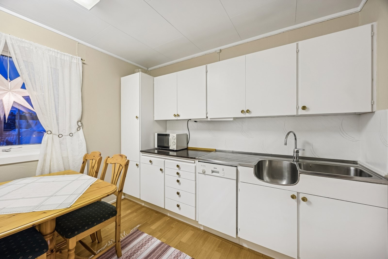 Kjøkkenet har en innredning med glatte hvite fronter og benkeplate i laminat med stålvask. Galleribilde