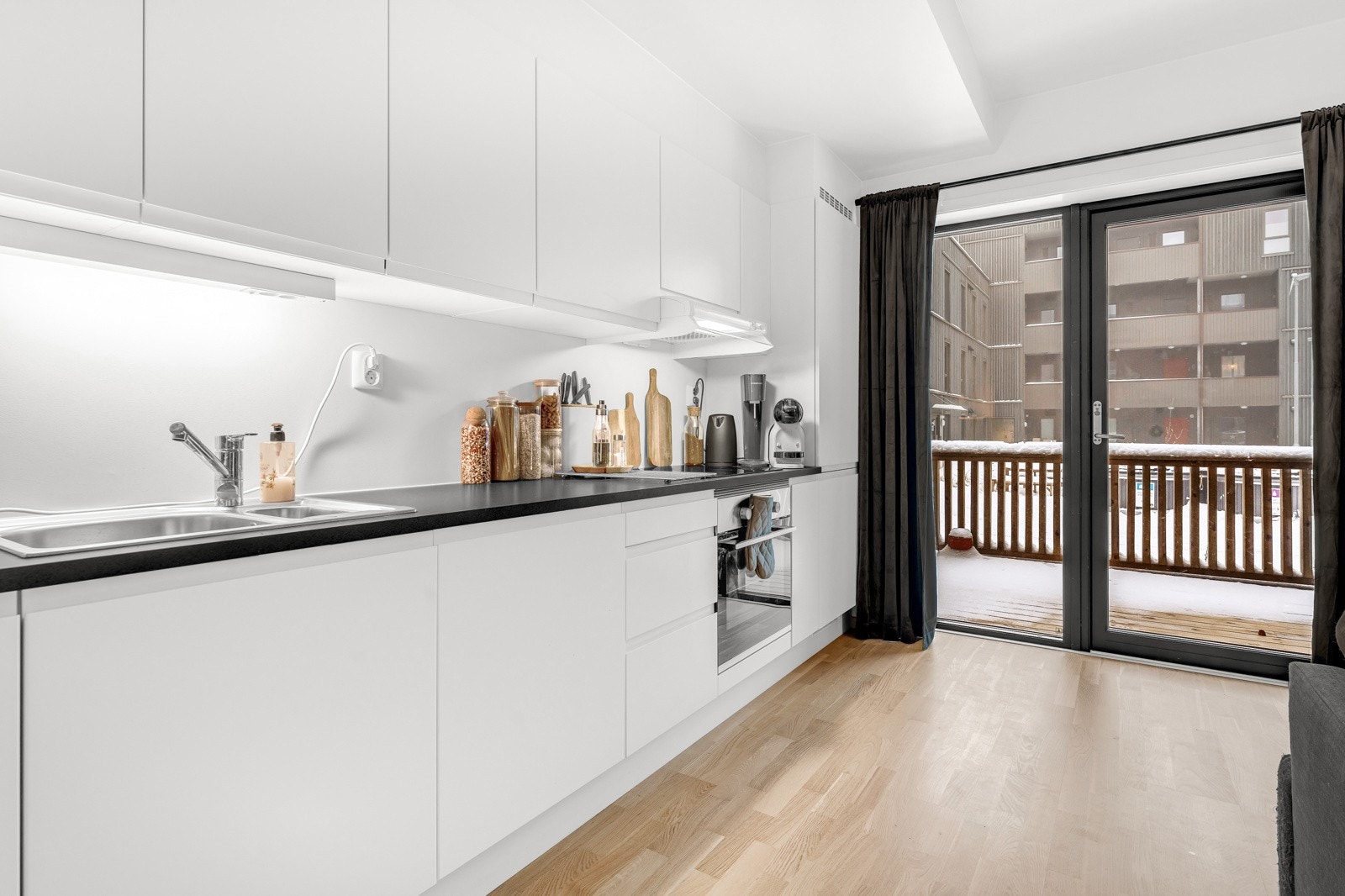 Innredningen har hvite glatte fronter og laminert benkeplate med nedfelt oppvaskkum. Praktisk med belysning under overskapene. Galleribilde