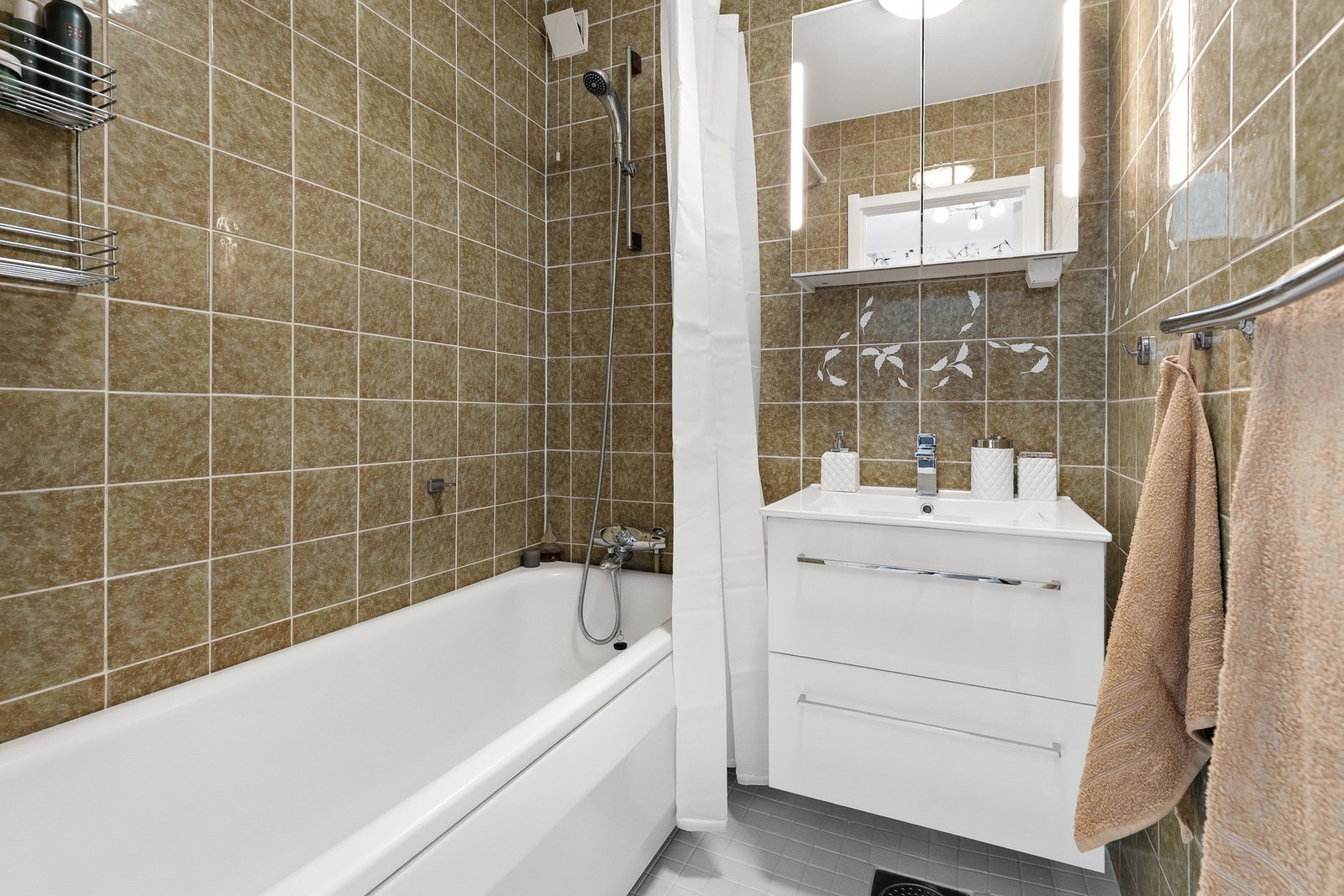 Rommet har gulvvarme og er innredet med badekar, servantinnredning og speilskap med sidelys Galleribilde