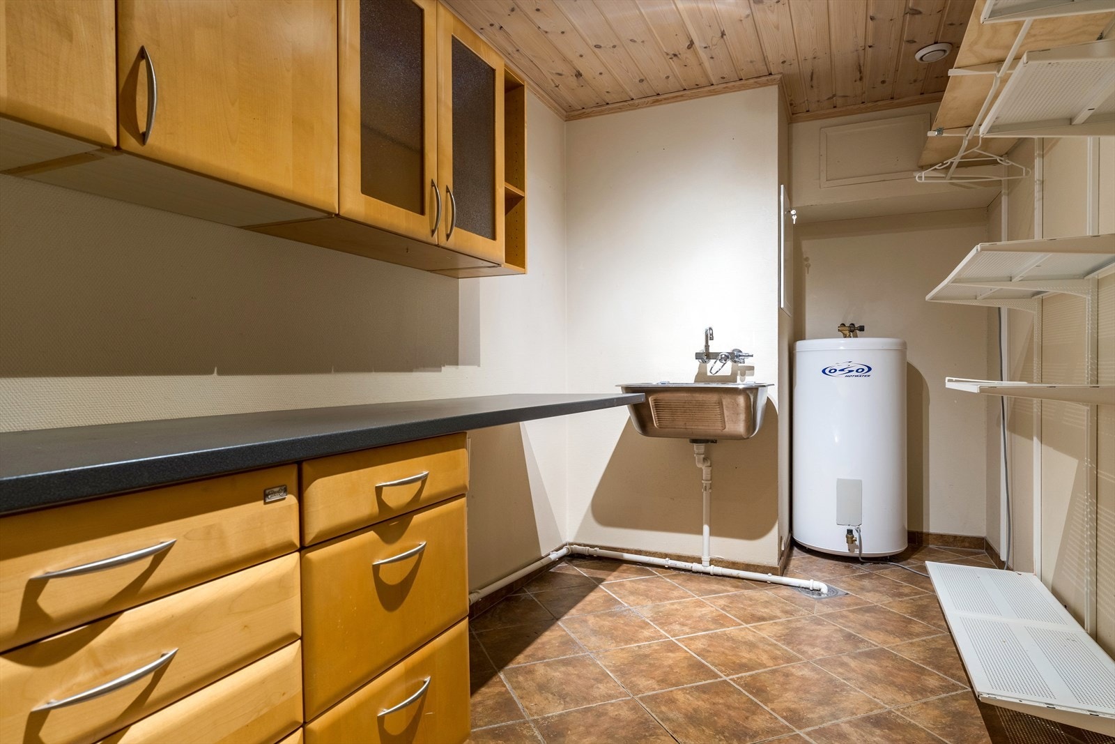 Praktisk vaskerom med flislagt gulv, innredning med over-og underskap, vaskekum og opplegg for vaskemaskin. Galleribilde