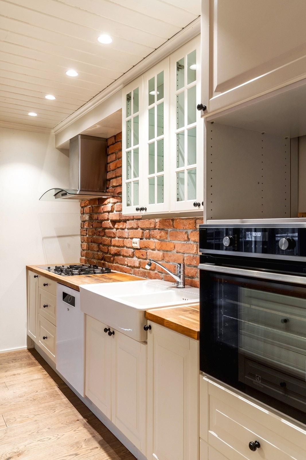 Kjøkkeninnredning med profilerte, lakkerte fronter og heltre benkeplate med nedfelt oppvaskkum. Ventilator med utluft og innfelte hvitevarer, inkludert stekeovn, gassplatetopp og oppvaskmaskin. Galleribilde