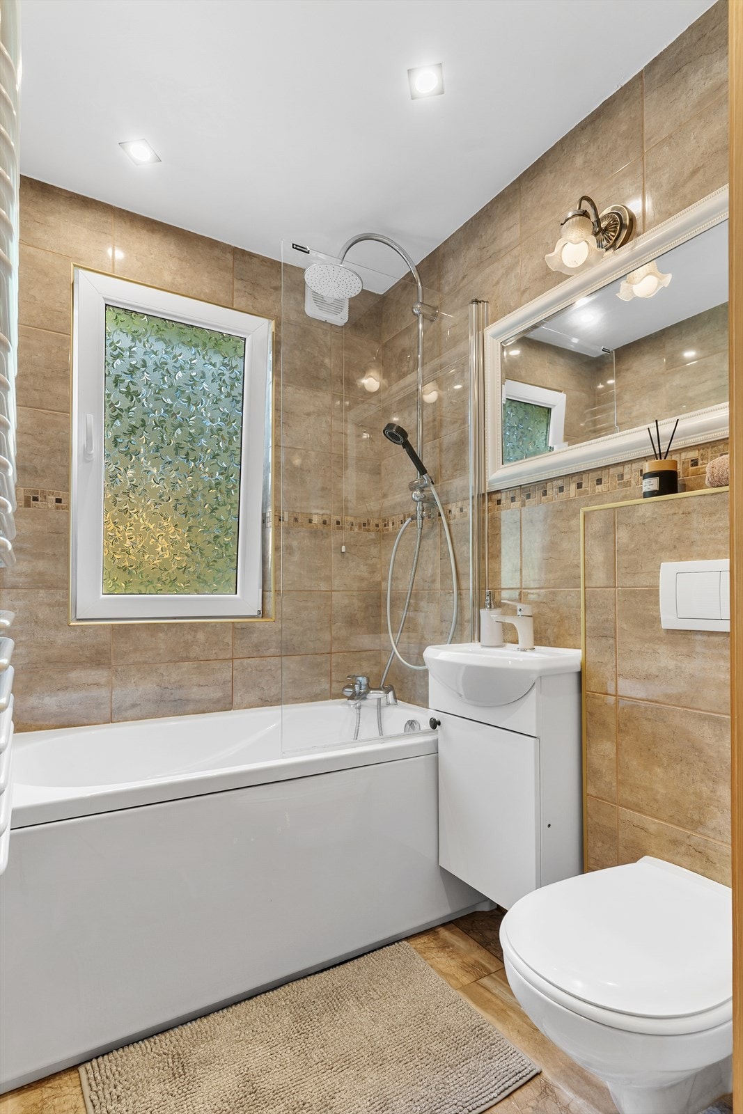 Badet har flislagte overflater i lune fargetoner og lyst interiør. Galleribilde