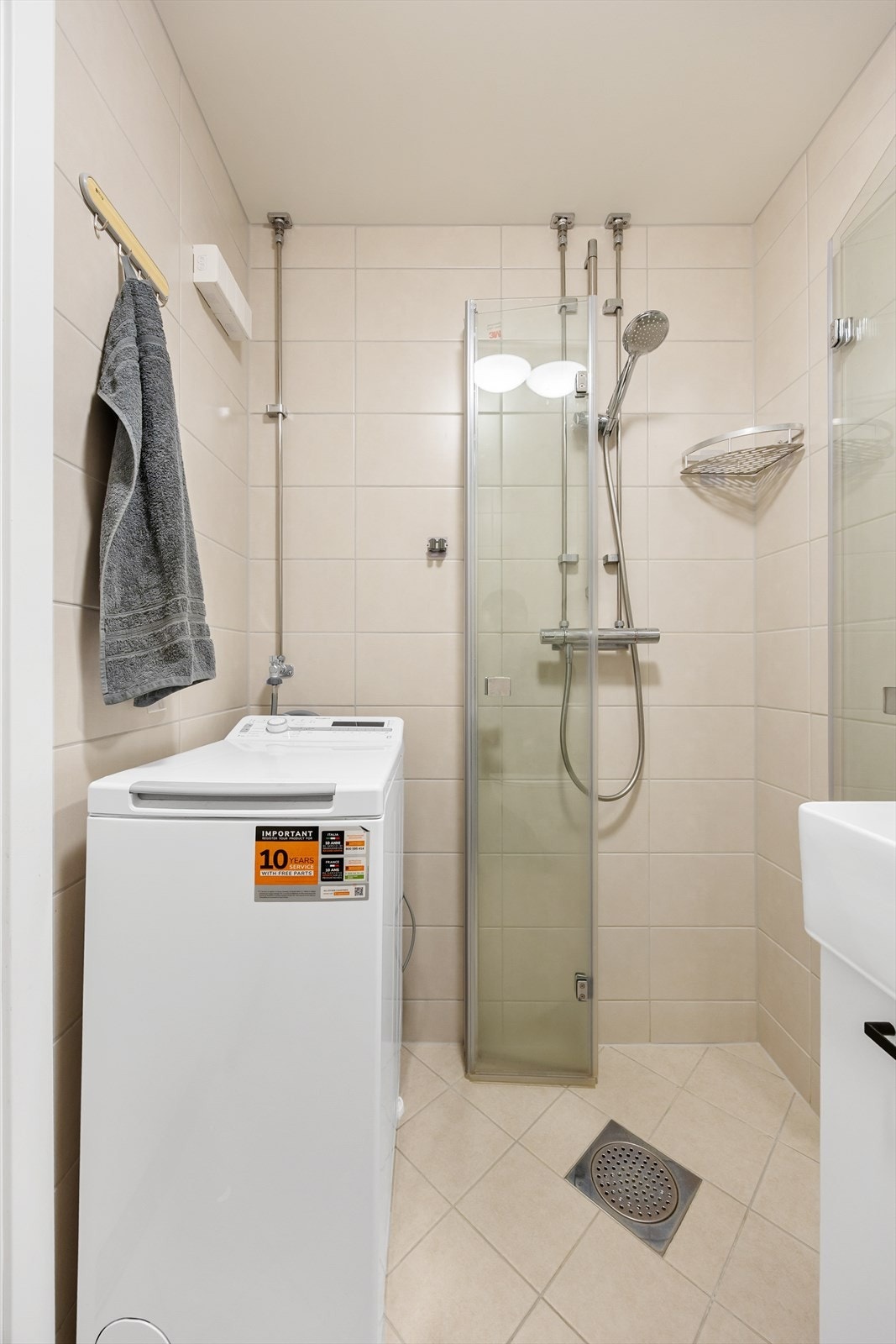 Badet er utstyrt med et stilrent dusjhjørne med glassdører og tilrettelagt for vaskemaskin Galleribilde