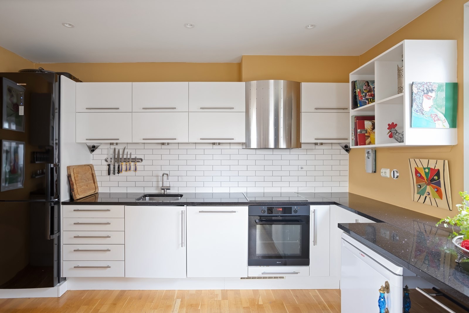 Pen kjøkkeninnredning fra 2003 med glatte folierte og høyglansfolierte fronter og benkeplate i steinkompositt med underlimt kum i rustfritt stål. Ventilator tilsluttet kanal/ventilasjonssystem. Galleribilde