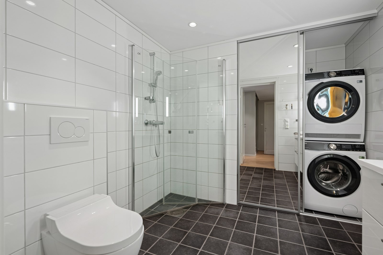 Rommet er utstyrt med vegghengt spyletoalett samt dusjhjørne med glassvegger. Bak to skyvedører med speilfronter ligger en egen vaskeromsdel, med opplegg for vaskemaskin samt plassering av kombinert ventilasjonsanlegg og varmtvannsbereder. Galleribilde