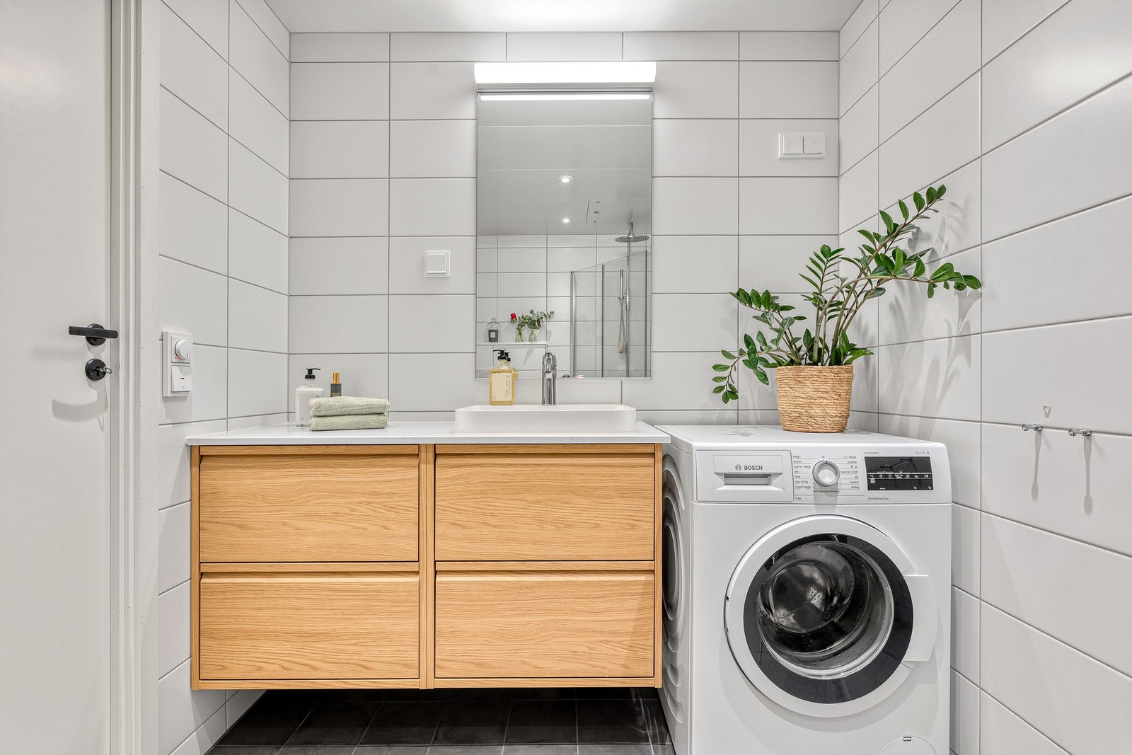 Badet har dusj med glassdører, veggmontert toalett og opplegg for vaskemaskin Galleribilde