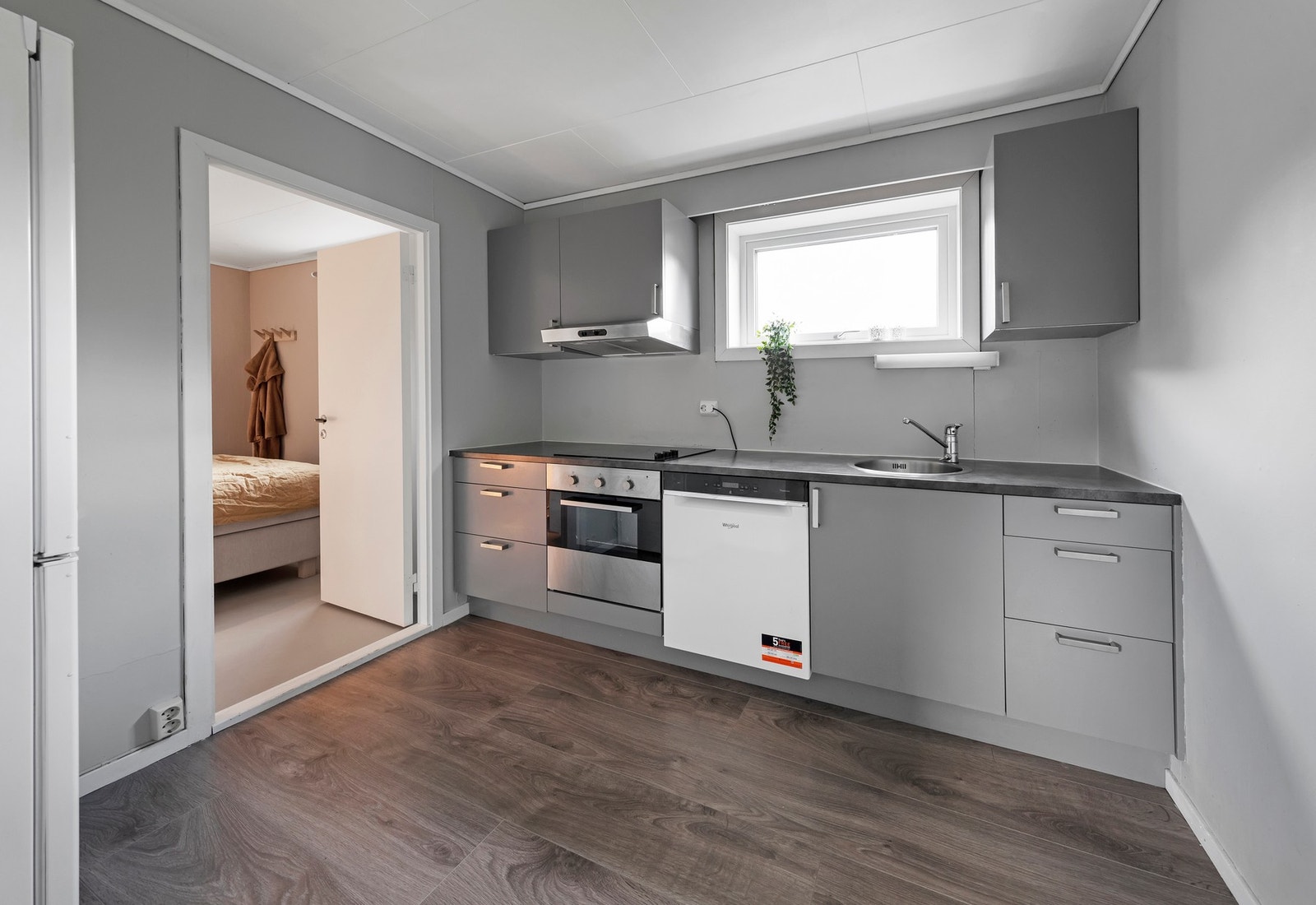 Kjøkken i sokkelleilighet har kjøkkeninnredning med malte fronter/dører, laminat benkeplater og integrerte hvitevarer som stekeovn, koketopp og oppvaskmaskin Galleribilde