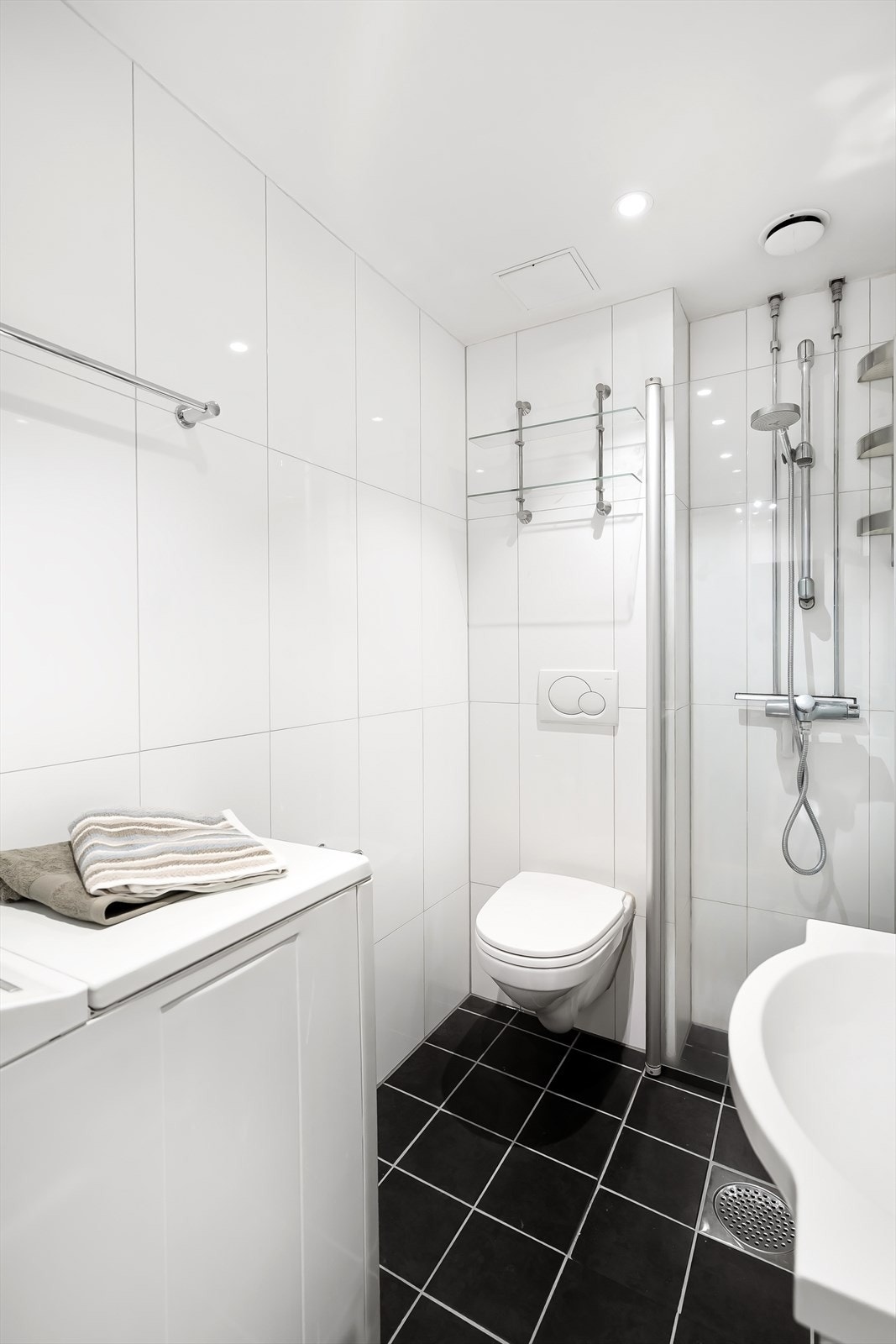 Badet er utstyrt med vegghengt servantinnredning med servant og ett-greps armatur, speilskap med overlys på vegg over servant og vegghengt toalett. Videre er det dusjsone med innfellbare dører av glass og metall og dusjarmatur tilkoblet hånddusj. Galleribilde