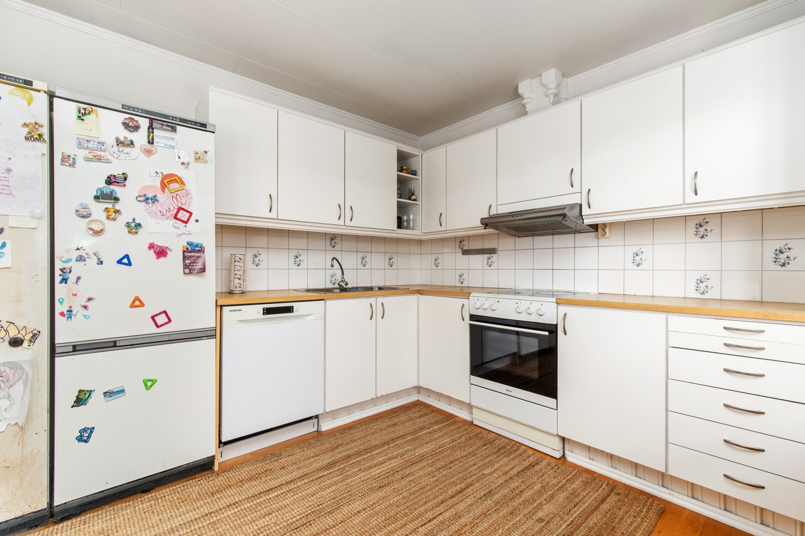 Kjøkkenet er innredet med klassisk kjøkkeninnredning med glatte fronter, laminert benkeplate og flis over benk. Galleribilde