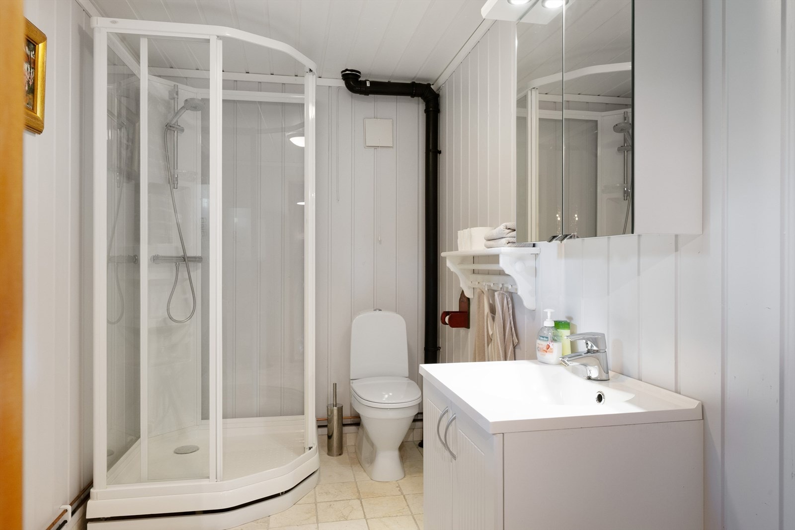 Badet har flislagte gulv, malt panel på vegger og i himling. Det er dusjkabinett, innredning med servant og toalett. Galleribilde