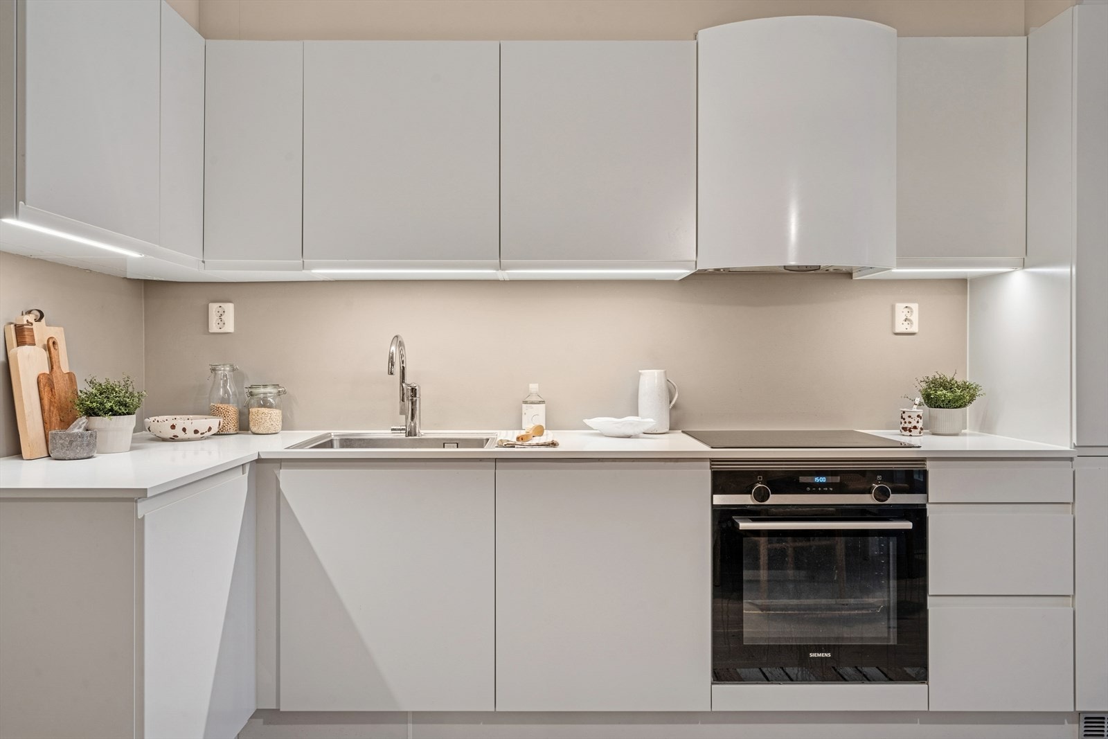 Lyslist under overskap, mekanisk vifte over integrert koketopp og ovn, laminert benkeplate, kum med ettgreps blandebatteri samt integrert kjøl/frys og oppvaskmaskin. Galleribilde