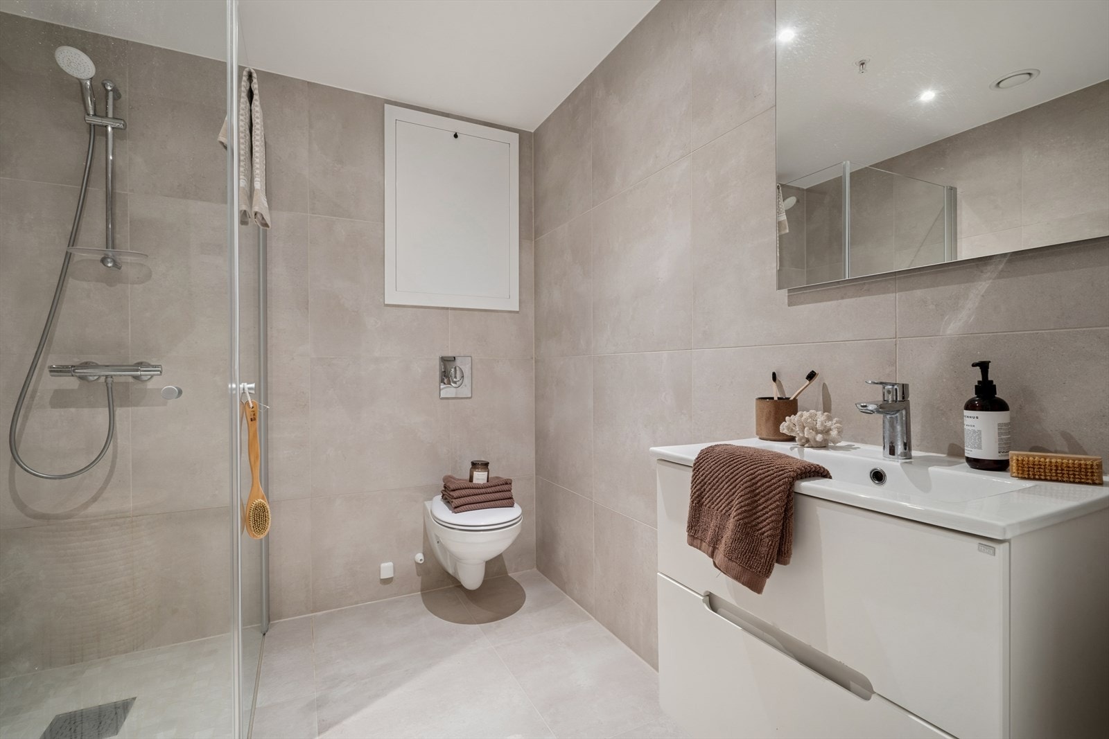 Veggmontert WC, dusj med inn- og utadslående glassvegger, servant med ettgreps blandebatteri i innredning og opplegg for vaskemaskin. Galleribilde