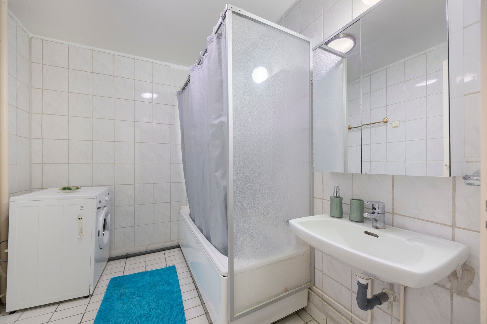 Badet er helfliset med slett hvitmalt tak. Det er ventilasjon til felles avtrekk og luftespalte i dør. Badet er innredet med badekar og benkeskap med servant. Det er også opplegg til vaskemaskin. Galleribilde