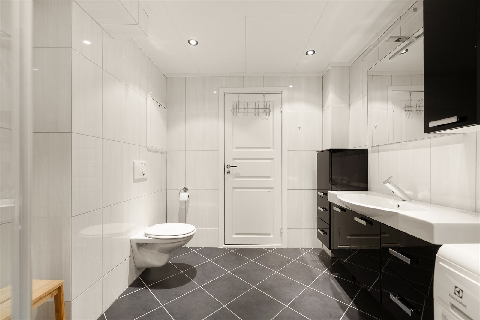 Badet har vegghengt toalett, servant med lagringsplass og speil, dusjhjørne med glassdører og opplegg til vaskemaskin. Galleribilde