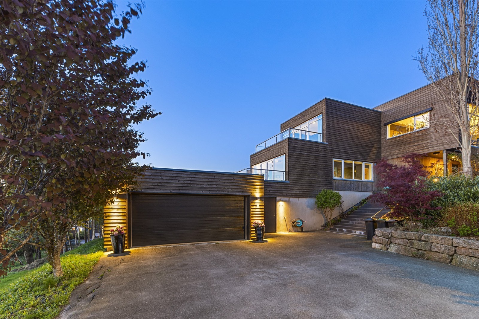 Stor garasje og rikelig med parkeringsmuligheter på tomten. Lekre beplantninger mot eiendommens inngangsparti. Galleribilde