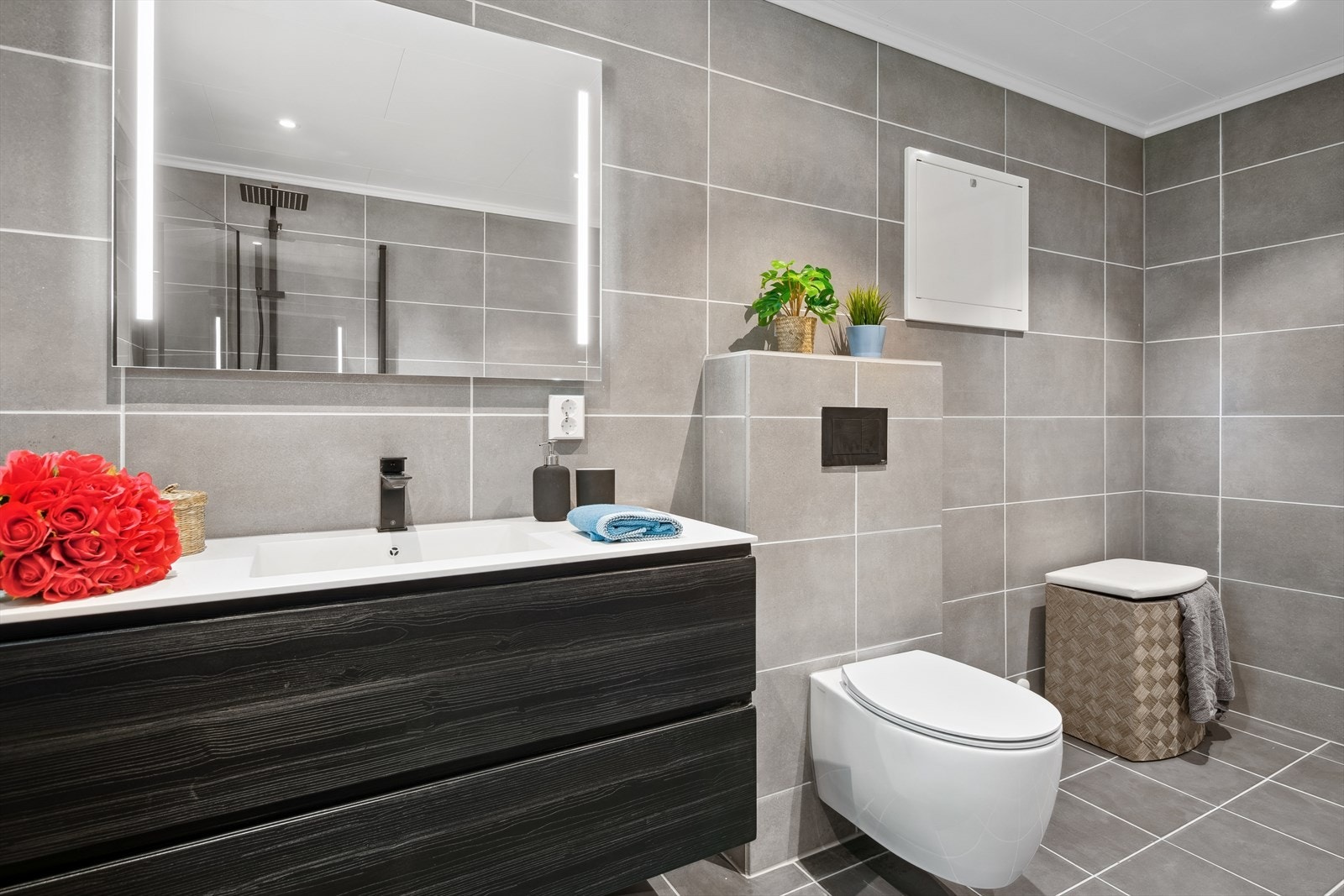 Det er vegghengt servantskap med overliggende servant i baderomsinnredning og vegghengt speil med integrert belysning. Galleribilde