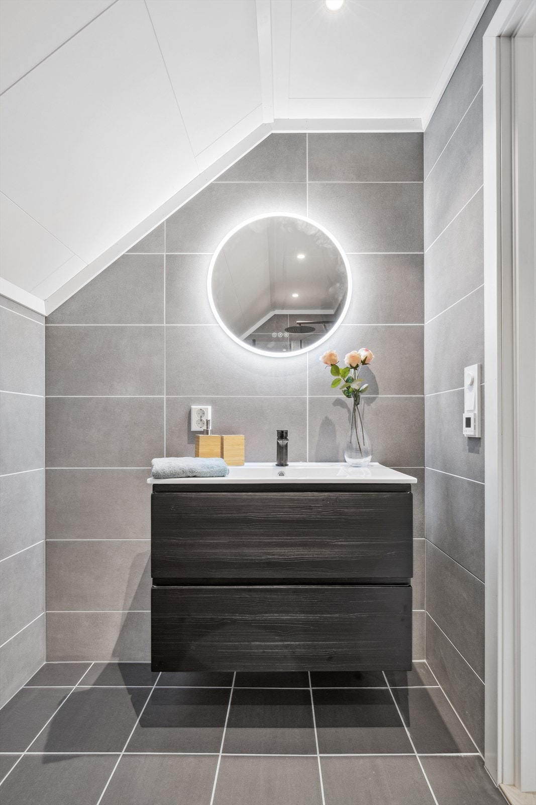 Intimt flislagt baderom fra 2025 med gulvvarme, downlights, vegghengt servantskap med overliggende servant i baderomsinnredning og vegghengt speil med integrert belysning. Galleribilde