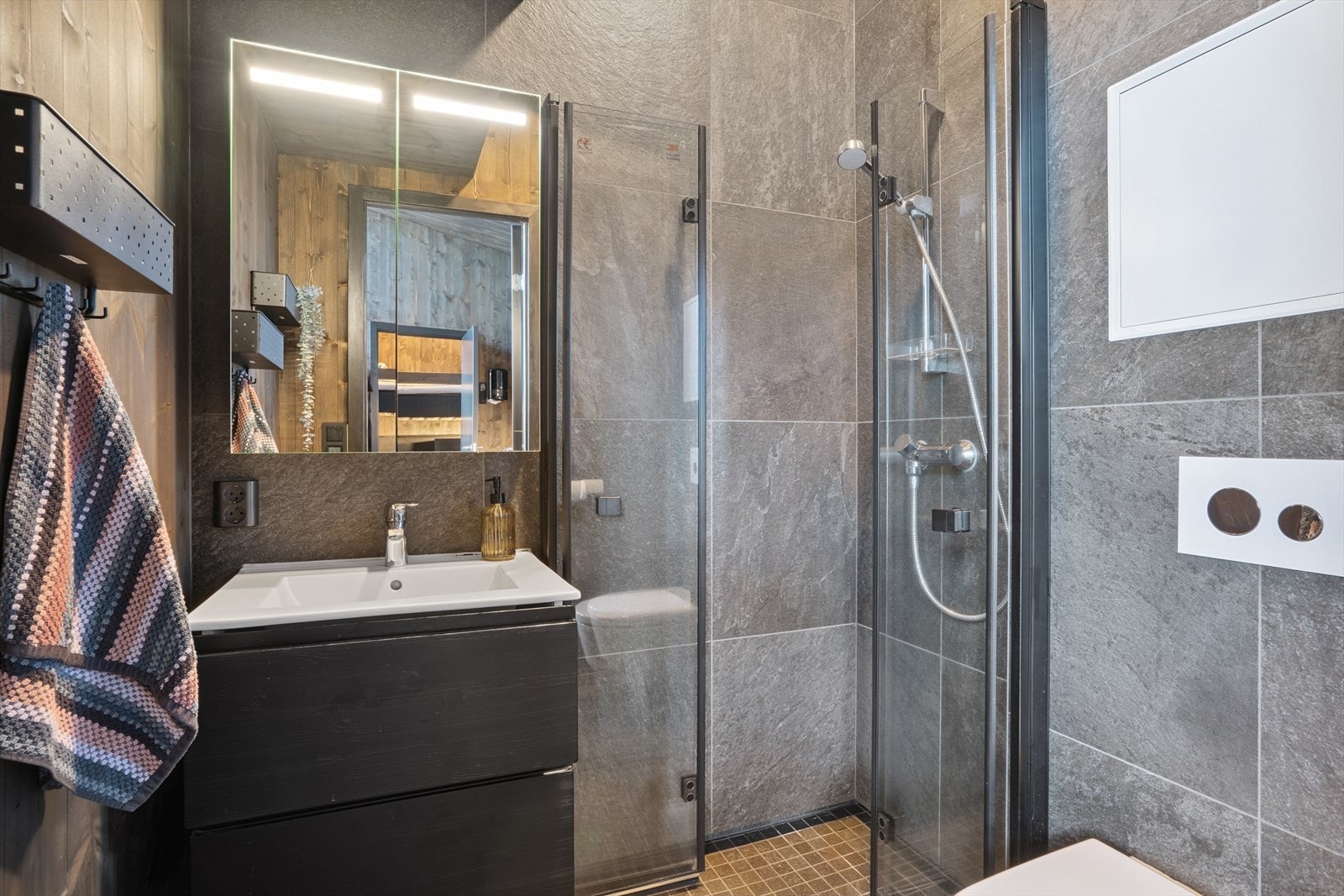 Flislagt baderom med gulvvarme og er utstyrt med servant i sort, slett baderomsinnredning, toalett og dusjhjørne med innfellbare glassvegger. Galleribilde