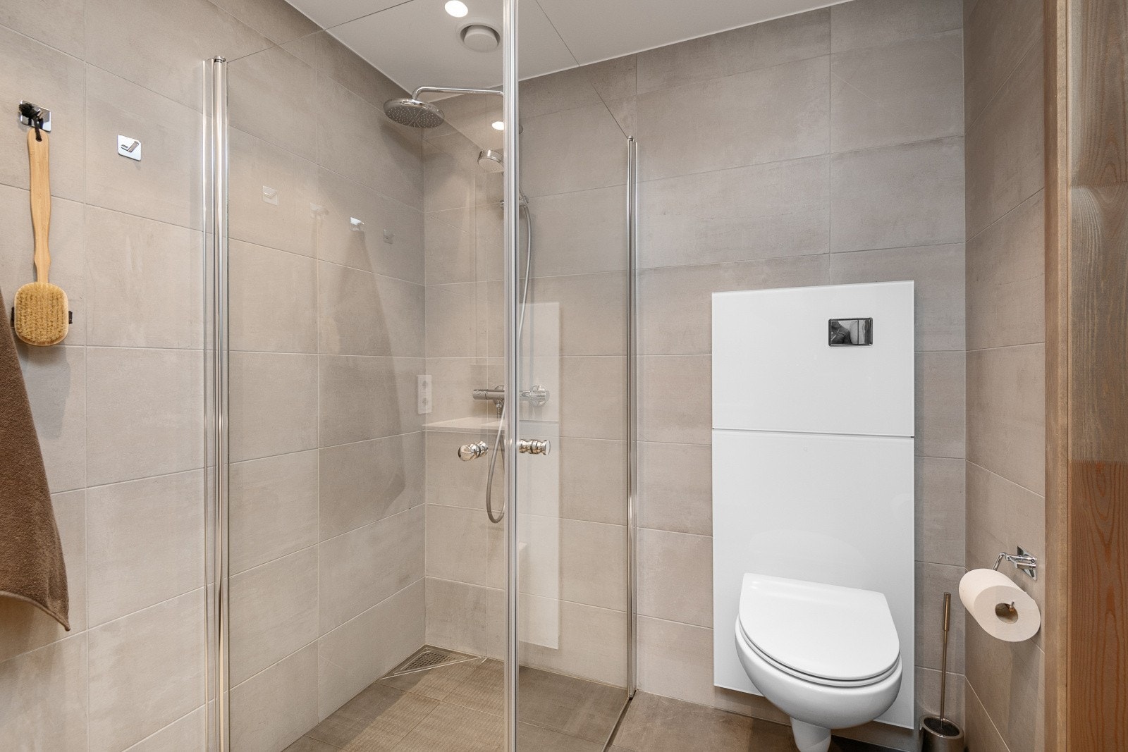 Badet er innredet med servant med underskap, speil med tilhørende belysning, dusjvegger, opplegg for vaskemaskin og vegghengt wc. Galleribilde