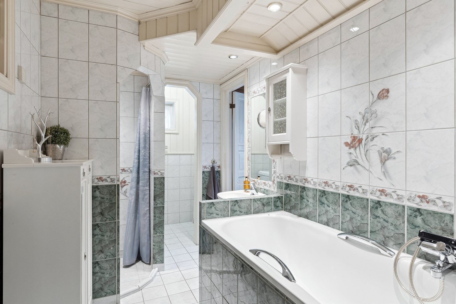 Bad/vaskerom med flislagt badekar, dusjnisje m/forheng, servant, innmurt speil, overskap, 2 frittstående skap, hyller og opplegg til vaskemaskin. Galleribilde