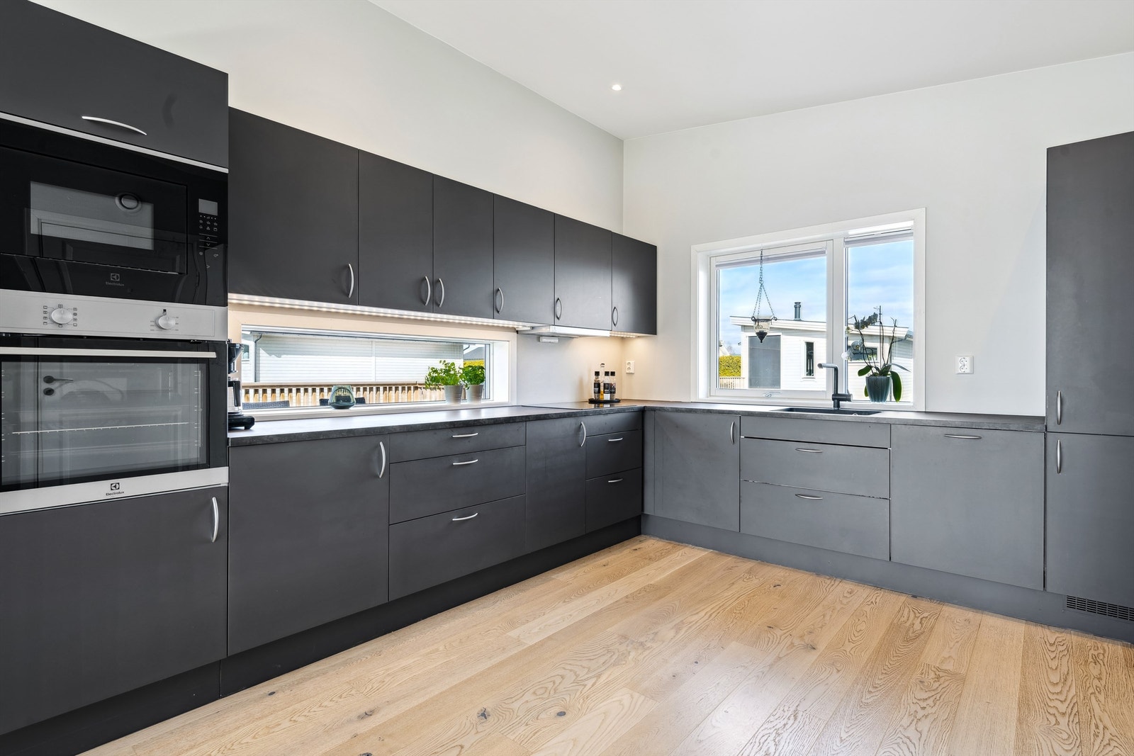 Pent kjøkken innredning i sorte malte glatte fronter, laminert benkeplate og integrerte hvitevarer Galleribilde