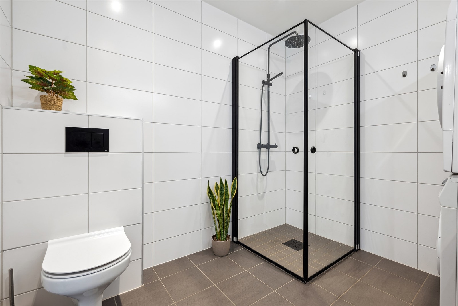 Det er innredet med vegghengt toalett og dusjnisje med glassdører med sorte detaljer Galleribilde