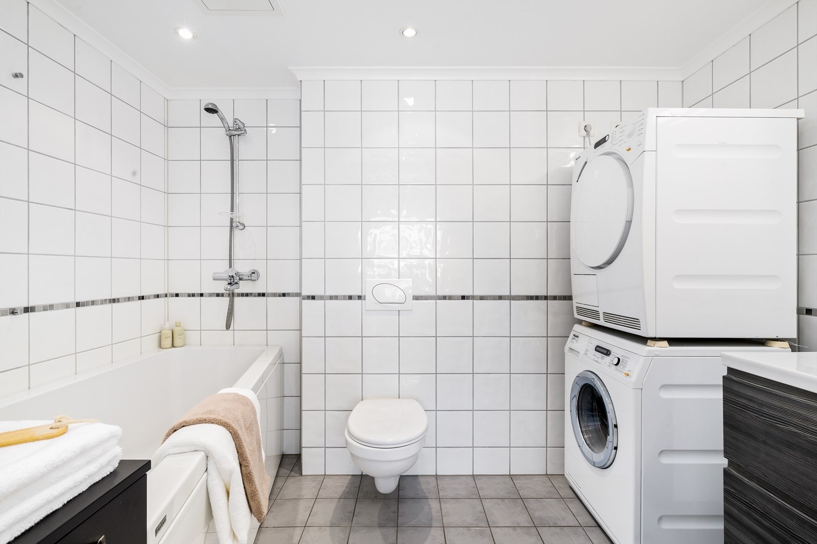 Rommet er innredet med veggmontert toalett, servant i stilren innredning, speil, badekar og opplegg for vaskemaskin. Galleribilde