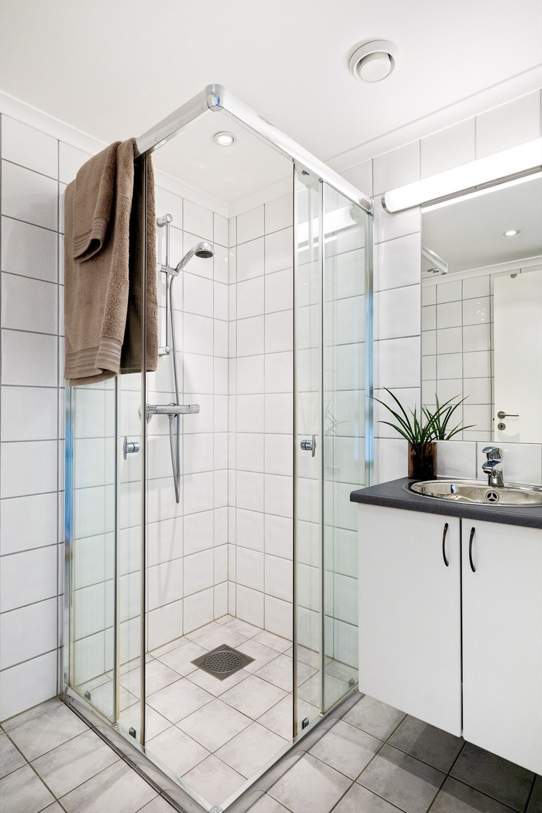 Rommet er innredet med en stilren baderomsinnredning med nedfelt servant, veggmontert toalett som gir et rent og moderne uttrykk, innmurt speil og et praktisk dusjhjørne. Galleribilde