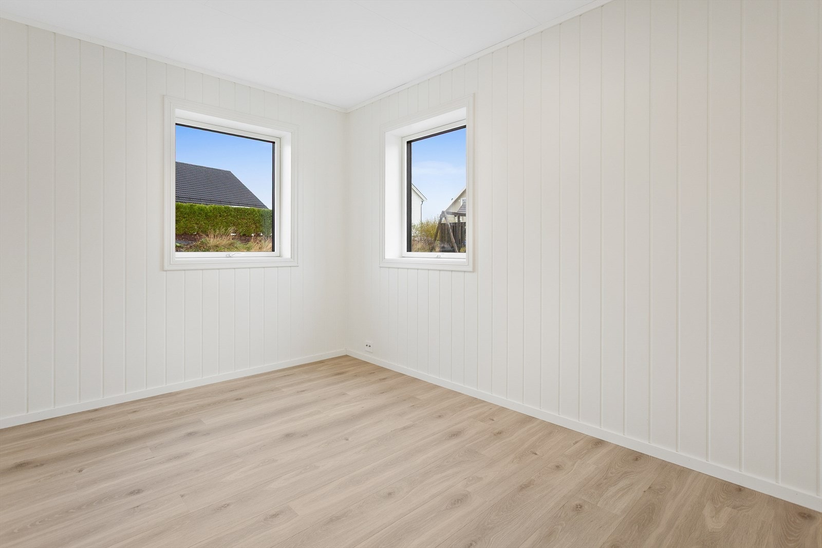 Rommet har lyse vegger og parkettgulv, med vinduer som gir utsikt til hagen. Galleribilde