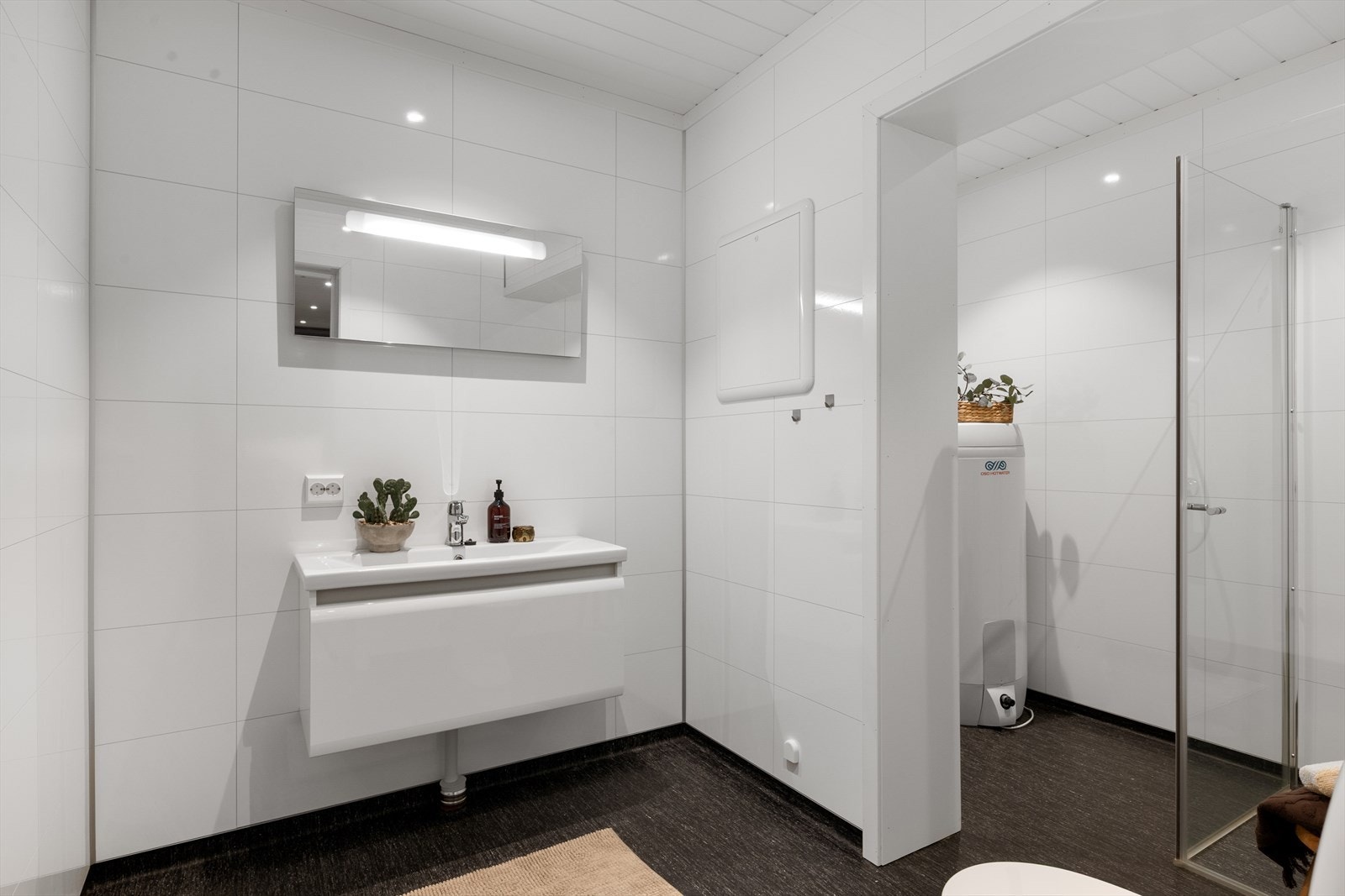 Badet har en tidløs utforming med lyse veggplater og mørkt gulvbelegg. Elektriske varmekabler i gulvet sørger for en lun og behagelig temperatur. Galleribilde