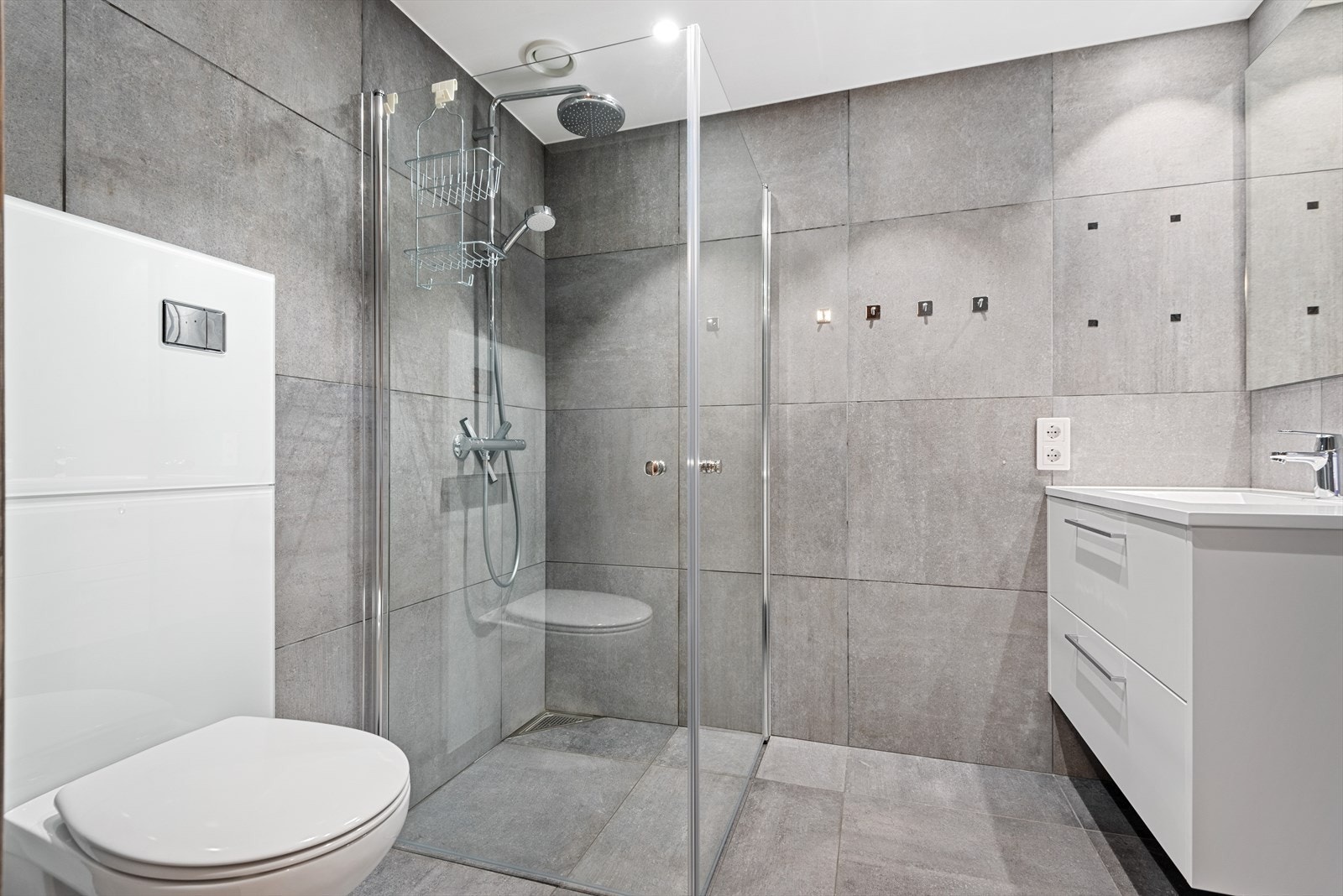Moderne bad med dusjhjørne, servantskap, vegghengt toalett og opplegg for vaskemaskin. Galleribilde