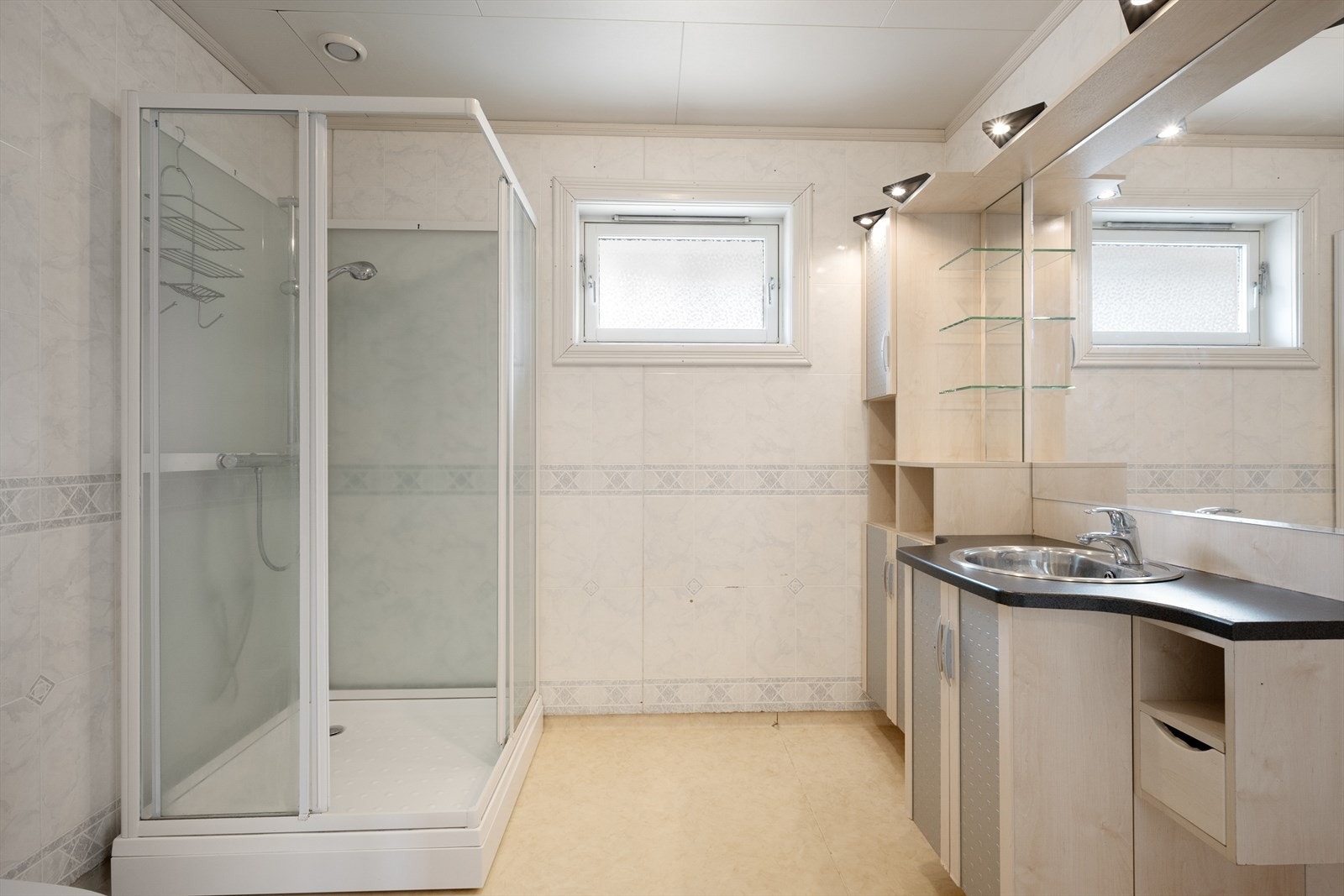 Rommet har plater på vegg og belegg på gulv, og er innredet med skapinnredning og dusjkabinett. Galleribilde