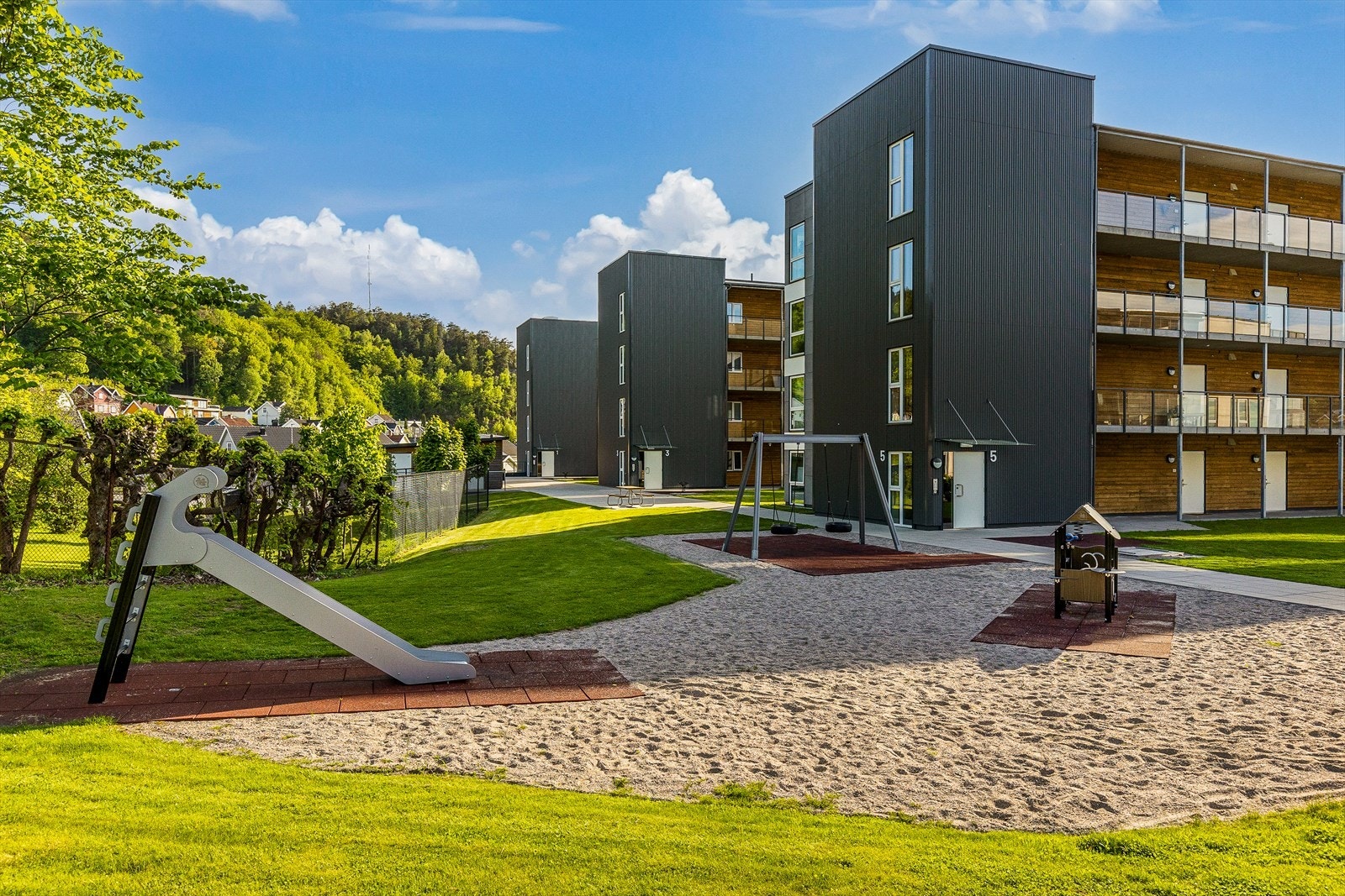 Mellom de fire byggene er det grønne og attraktive utearealer med busker, beplantning, lekeapparater, bord og benker Galleribilde