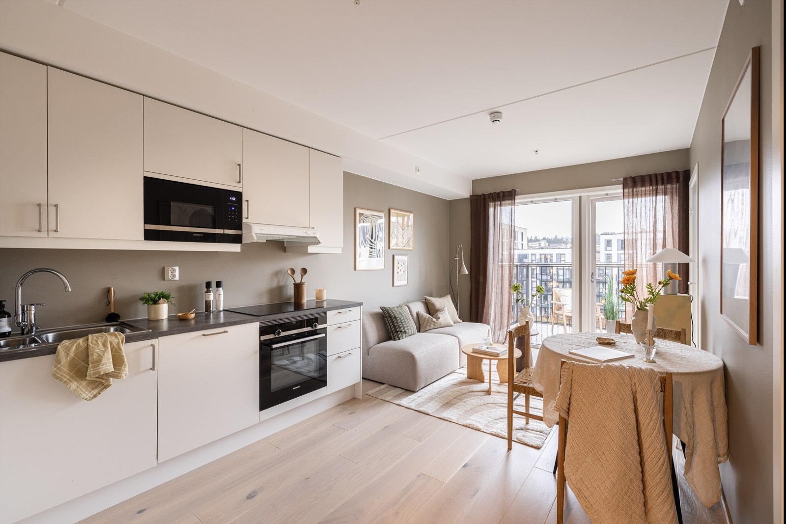 Lys og romslig stue med naturlig sonedeling mot kjøkkenet. De store vinduene skaper en varm og åpen atmosfære. Galleribilde