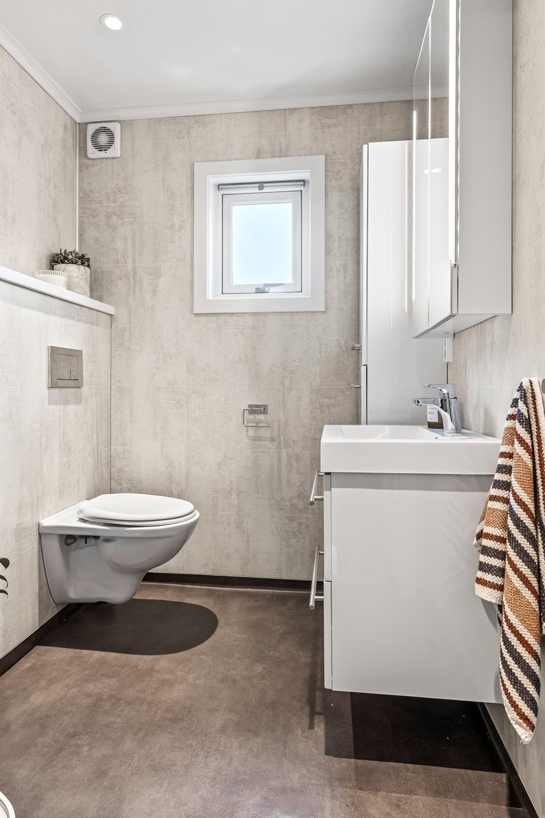 Pent og moderne bad med våtromsplater på veggene, vegghengt toalett og servantskap. Galleribilde