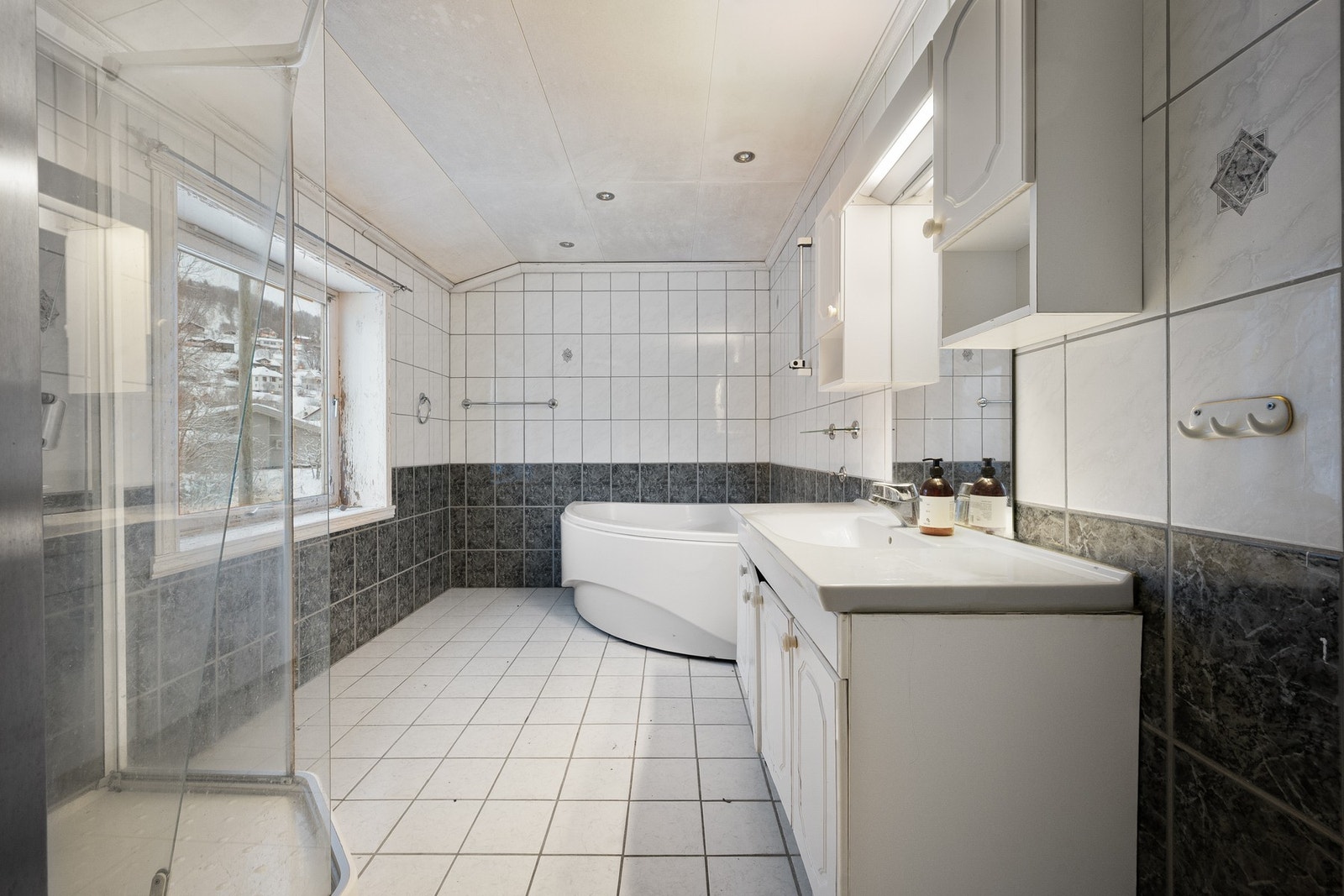 Flislagt bad av god størrelse med badekar, servantinnredning, dusjkabinett og toalett Galleribilde