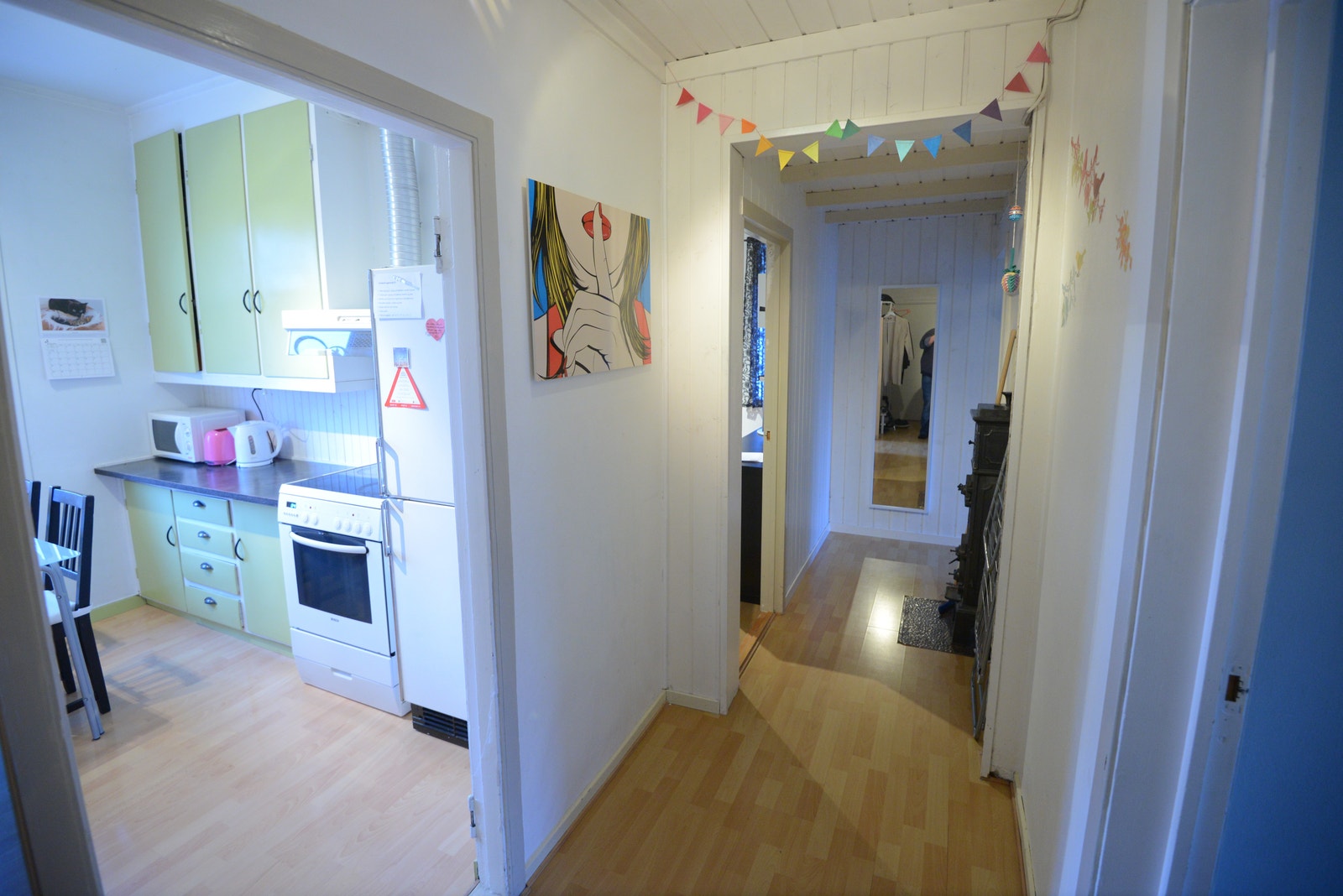 Gang mellom kjøkken og hyblene, hvor kakkelovn varmer en kald vinterdag. Galleribilde