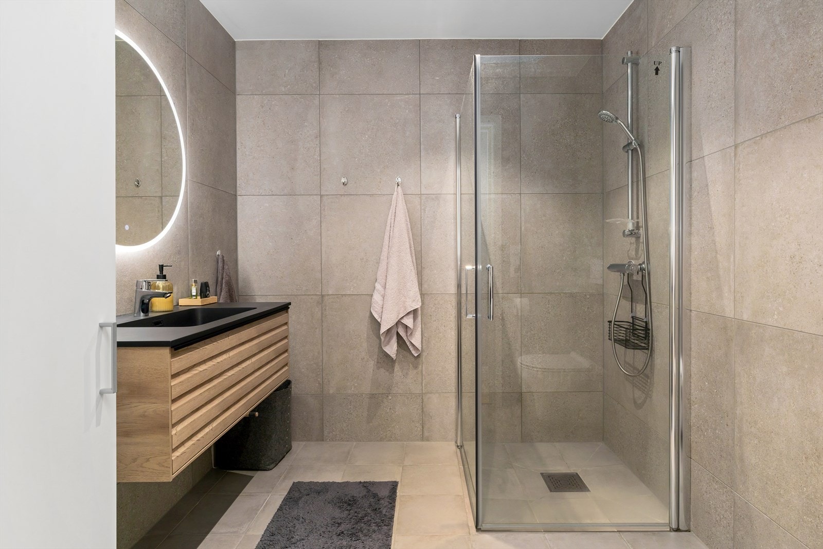 Delikat bad hvor veggene og gulvet er kledd med store, grå fliser(fra Modena) som gir et tidløst og luksuriøst uttrykk. Det er varmekabler på badet. Galleribilde