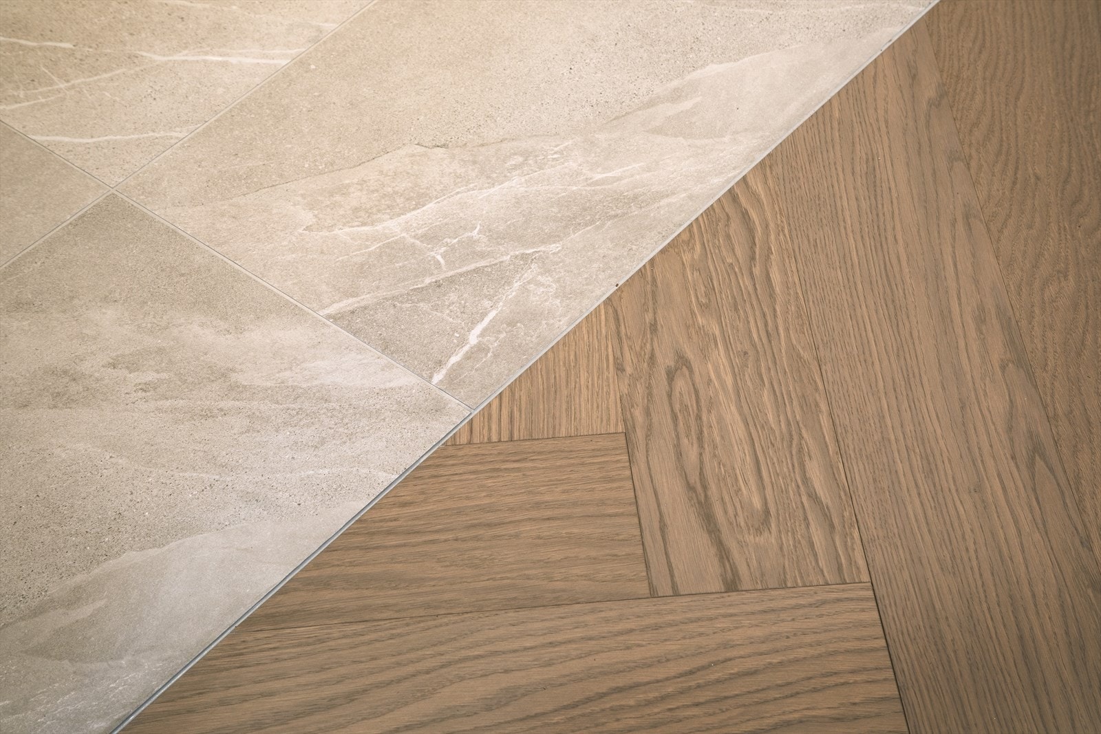 Fliser som møter herdet eikegulv lagt i elegant fiskebeinsmønster gir en ren og markert overgang. Det er varme i gulv i gangen. Galleribilde