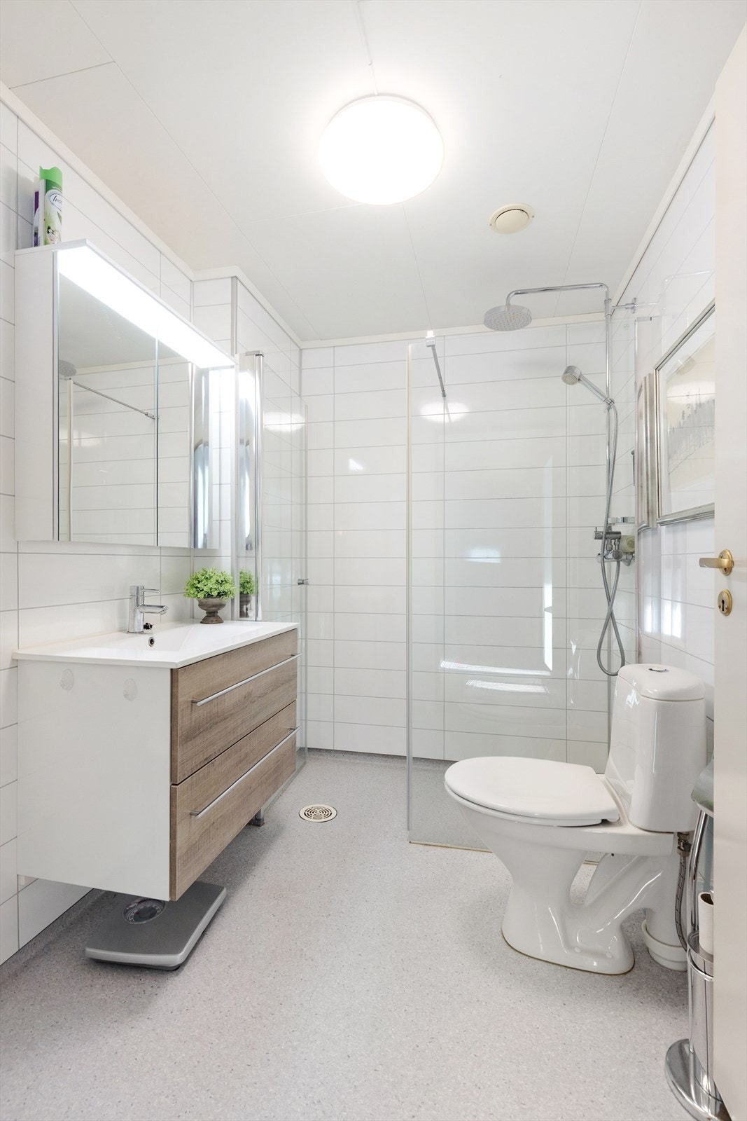 Badet fra 2019 har også en lys fargepalett, med belegg på gulv med varmekabler og baderomsplater på veggene. Badet har en moderne innredning med dype skuffer og heldekkende servant, samt speilskap. Badet er også innredet med dusjnisje og toalett. Galleribilde